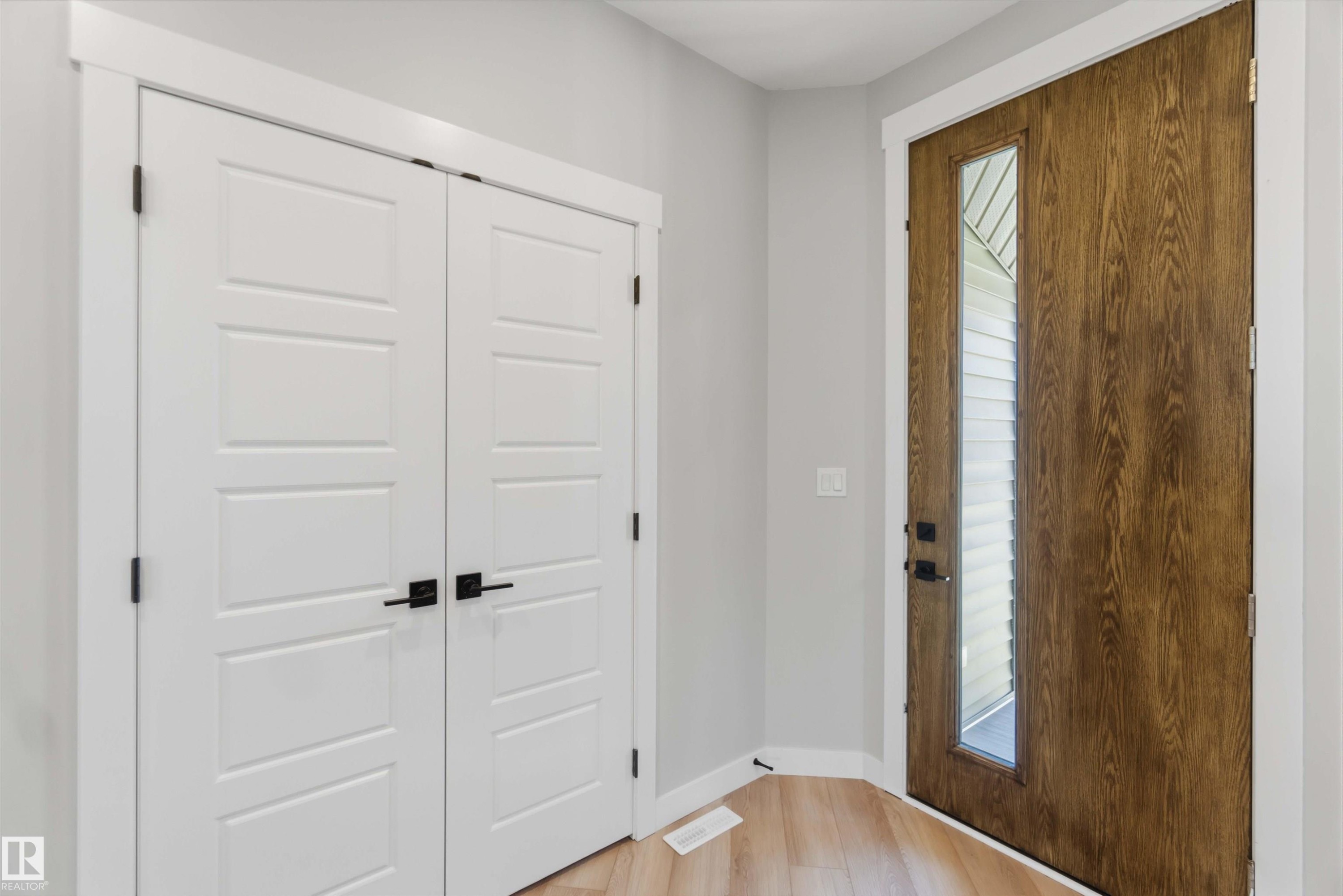 Wood-finish flooring, white paneled doors with matte black hardware, and a wood-finish entry door with a vertical glass insert - 28 Harley Way, Spruce Grove, AB - Indoor Photo Showing Other Room