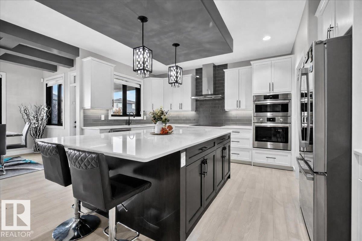 Expansive kitchen island with a white countertop, two pendant lights, stainless steel appliances, and white cabinetry - 6813 Knox Loop Sw, Edmonton, AB - Indoor Photo Showing Kitchen With Upgraded Kitchen