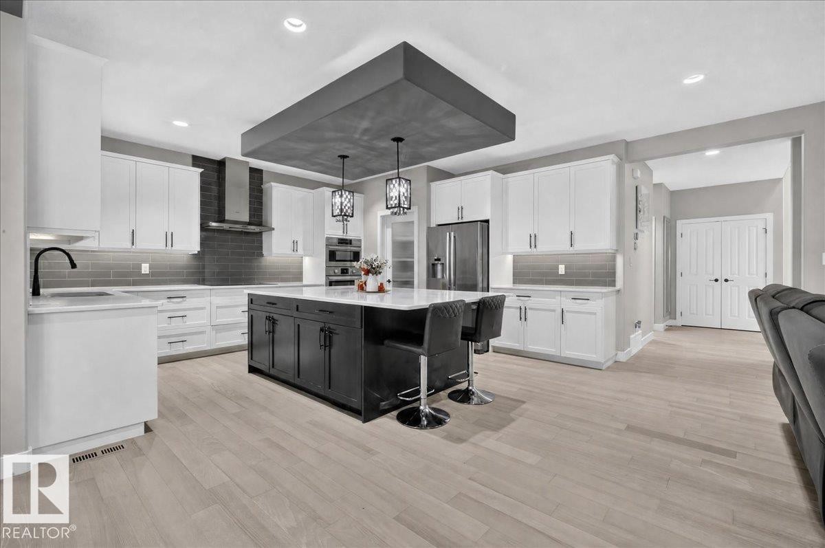Gourmet kitchen featuring a large central island with pendant lighting, stainless steel appliances, extensive white cabinetry, and light wood-finish flooring - 6813 Knox Loop Sw, Edmonton, AB - Indoor Photo Showing Kitchen With Upgraded Kitchen