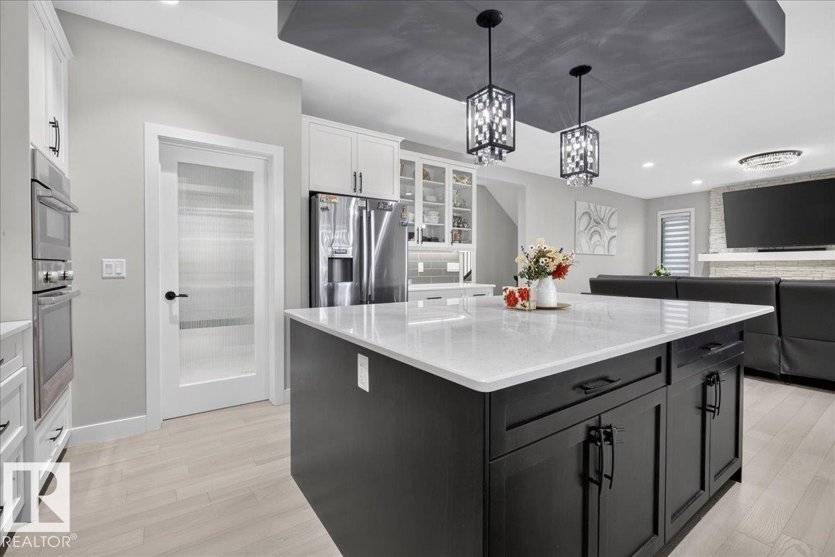 Kitchen island with light-toned countertop, dark cabinetry, and pendant lighting - 6813 Knox Loop Sw, Edmonton, AB - Indoor Photo Showing Kitchen With Upgraded Kitchen