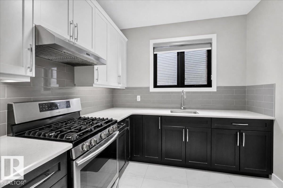 Two-tone cabinetry with white upper and dark lower units, stainless steel range with overhead vent, gray subway tile backsplash, and light countertops - 6813 Knox Loop Sw, Edmonton, AB - Indoor Photo Showing Kitchen With Upgraded Kitchen