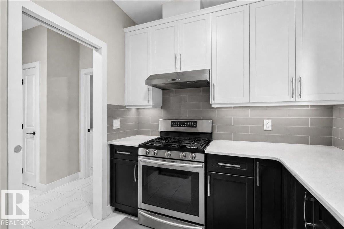 White upper cabinetry, dark lower cabinetry, light-toned countertops, subway tile backsplash, and stainless steel gas range with exhaust hood - 6813 Knox Loop Sw, Edmonton, AB - Indoor Photo Showing Kitchen