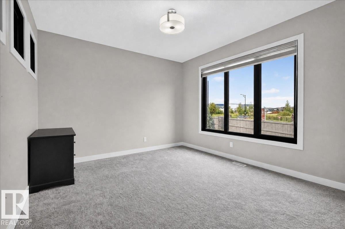 Neutral wall paint, ceiling-mounted light fixture, large picture window with black framing, white window trim, and grey carpeting - 6813 Knox Loop Sw, Edmonton, AB - Indoor Photo Showing Other Room