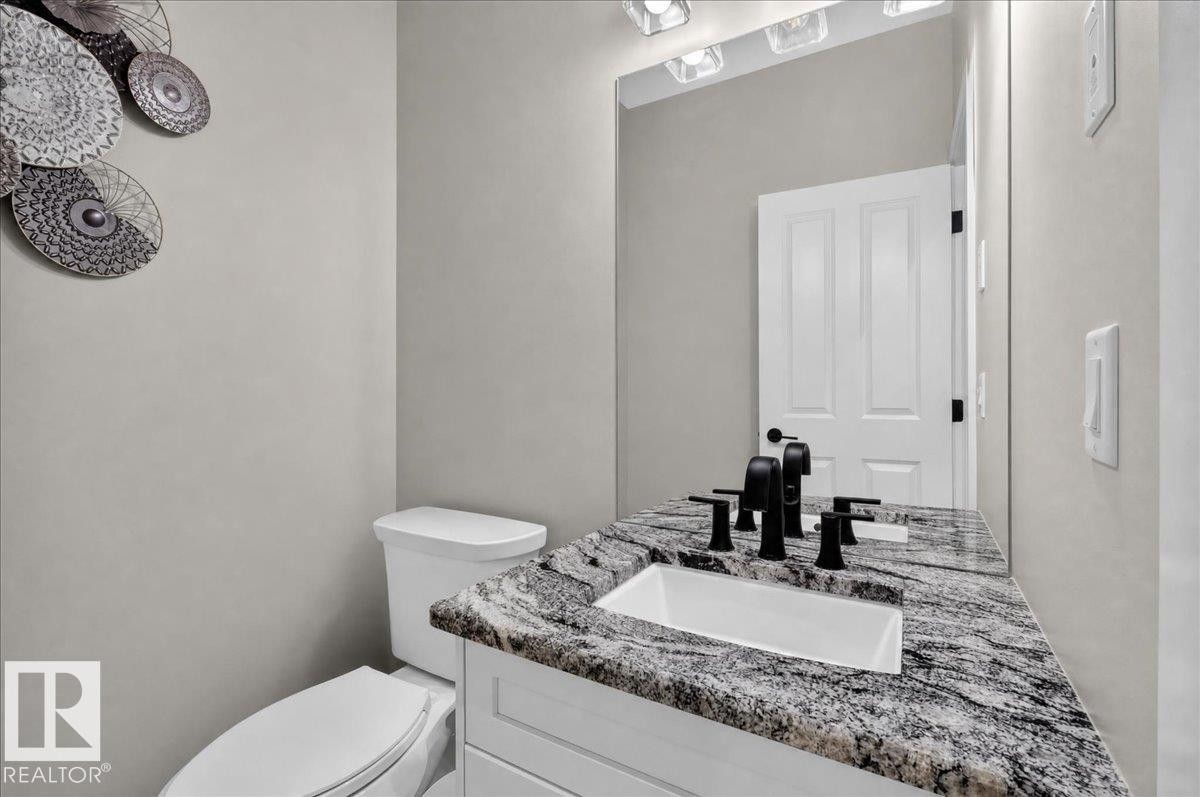 Vanity with a speckled countertop and integrated sink, matte black fixtures, and a wall-mounted mirror with overhead lighting - 6813 Knox Loop Sw, Edmonton, AB - Indoor Photo Showing Bathroom