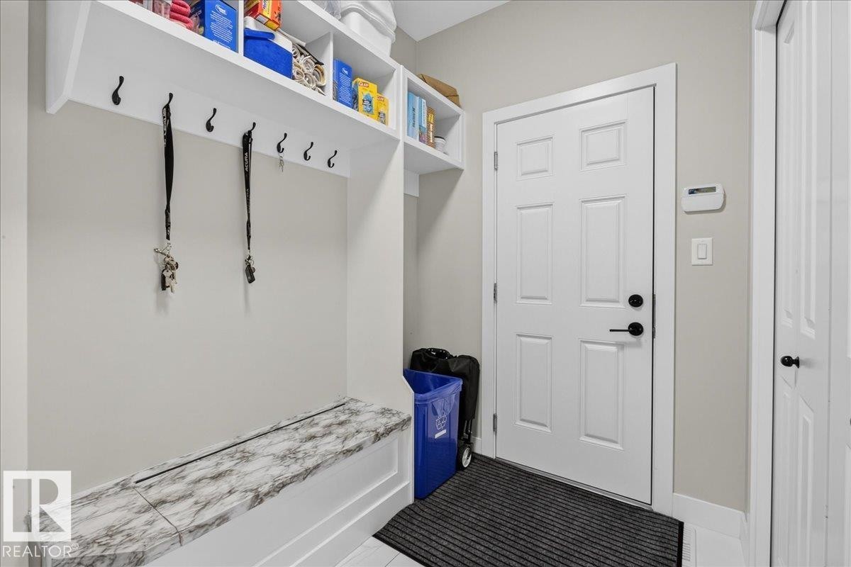 Built-in storage bench with a marbled top, white paneled door, and overhead shelving with integrated hooks - 6813 Knox Loop Sw, Edmonton, AB - Indoor Photo Showing Other Room