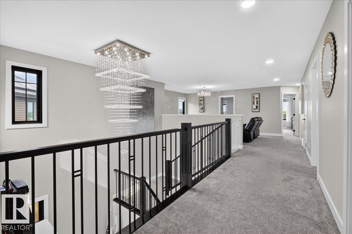 Modern chandelier, black wrought iron railing, light gray wall paint, recessed lighting, gray carpeting - 6813 Knox Loop Sw, Edmonton, AB - Indoor Photo Showing Other Room