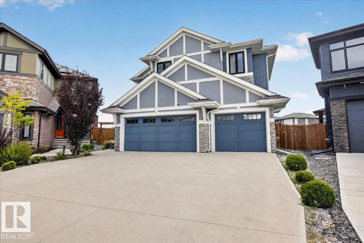 Modern exterior with multiple gables, gray siding, stone accents, two garage doors, and a concrete driveway - 6813 Knox Loop Sw, Edmonton, AB - Outdoor With Facade