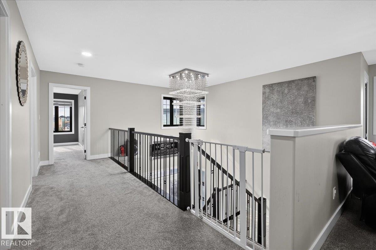 Plush carpeted flooring, metal baluster railing, and a multi-tiered chandelier - 6813 Knox Loop Sw, Edmonton, AB - Indoor Photo Showing Other Room