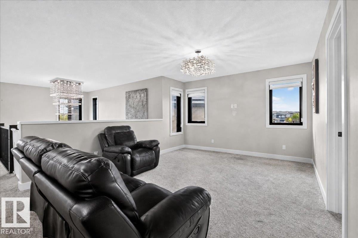 Carpeted open-concept bonus room featuring two distinct crystal chandeliers and multiple windows - 6813 Knox Loop Sw, Edmonton, AB - Indoor
