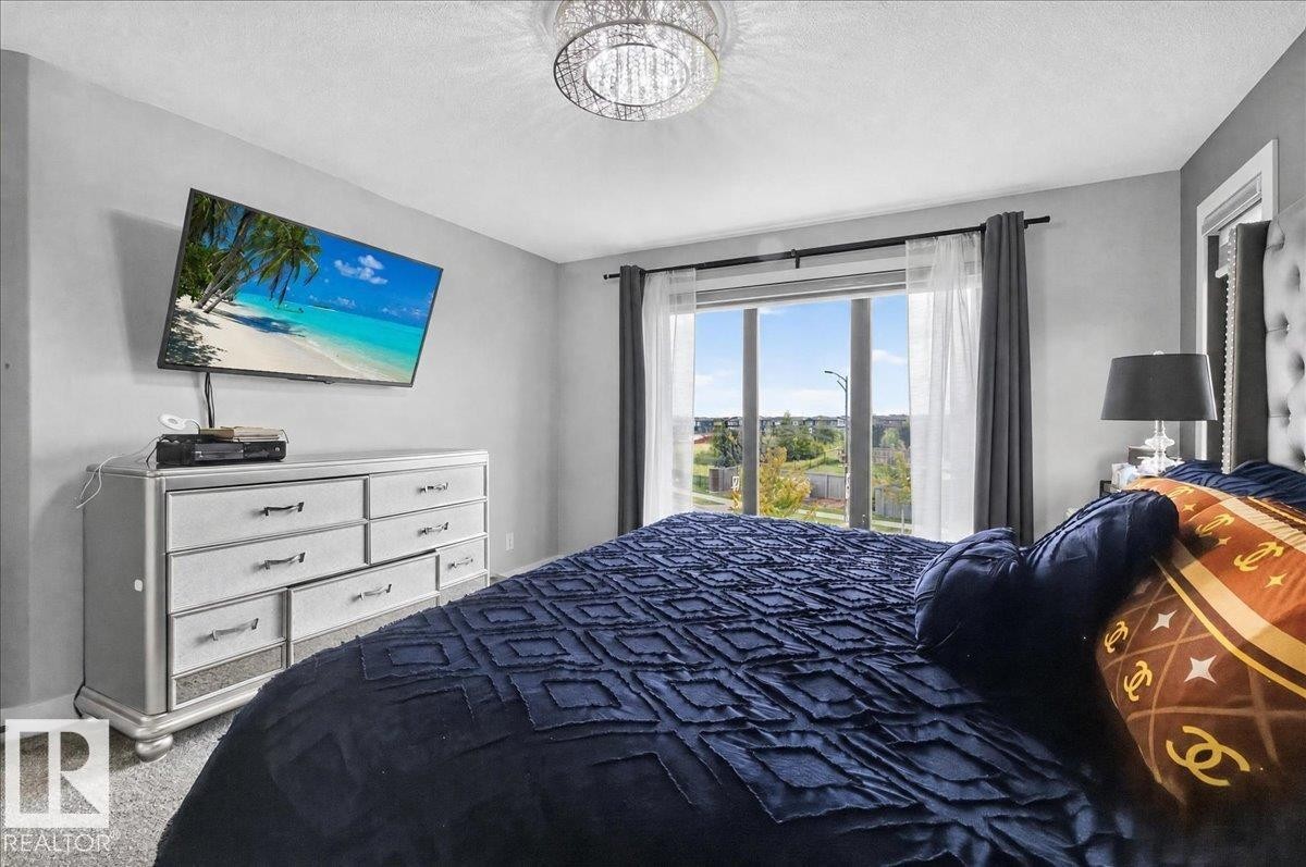Large window with abundant natural light, grey carpet, and a decorative ceiling light fixture - 6813 Knox Loop Sw, Edmonton, AB - Indoor Photo Showing Bedroom