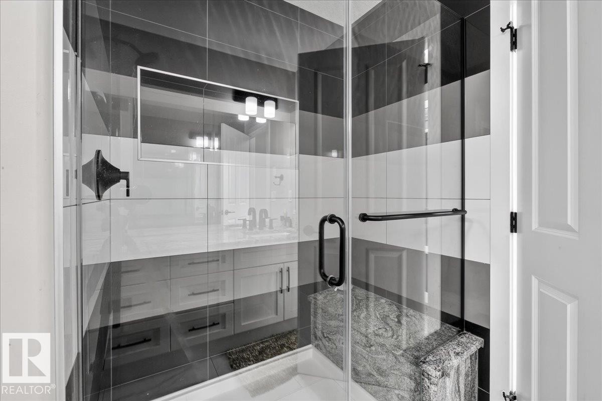 Glass-enclosed shower with horizontal striped tiling, a built-in stone bench, and matte black hardware - 6813 Knox Loop Sw, Edmonton, AB - Indoor Photo Showing Bathroom