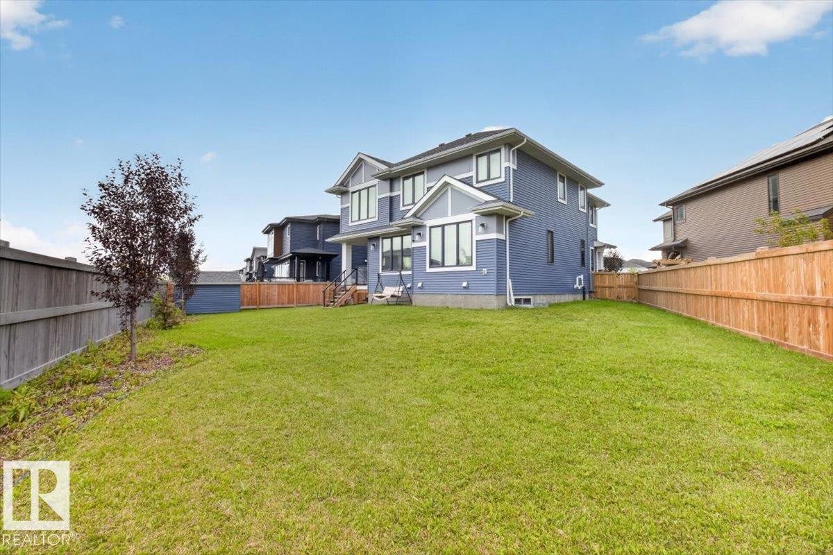 Expansive rear yard with a manicured lawn, full privacy fencing, and exterior lighting fixtures - 6813 Knox Loop Sw, Edmonton, AB - Outdoor