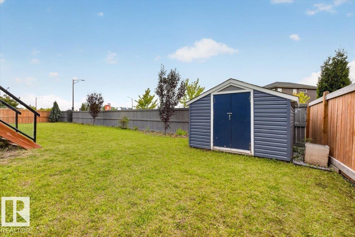 Expansive backyard featuring a manicured lawn, a blue storage shed with double doors, a wood privacy fence, and an additional gray fence - 6813 Knox Loop Sw, Edmonton, AB - Outdoor