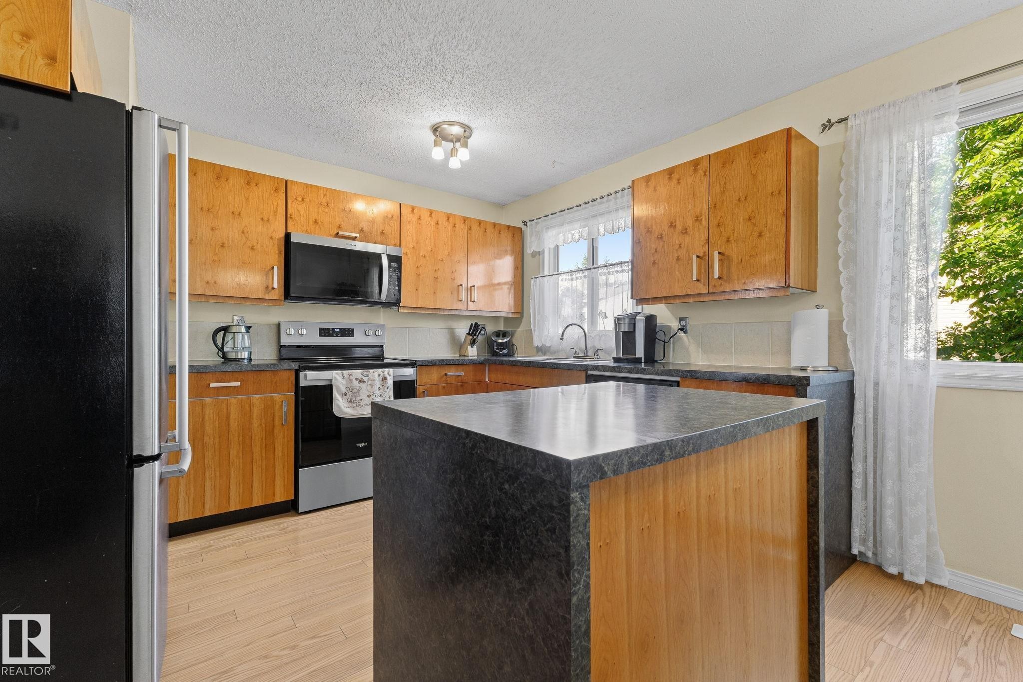 Wood-finish flooring with a central island featuring a dark countertop - 17132 103 Street Nw, Edmonton, AB