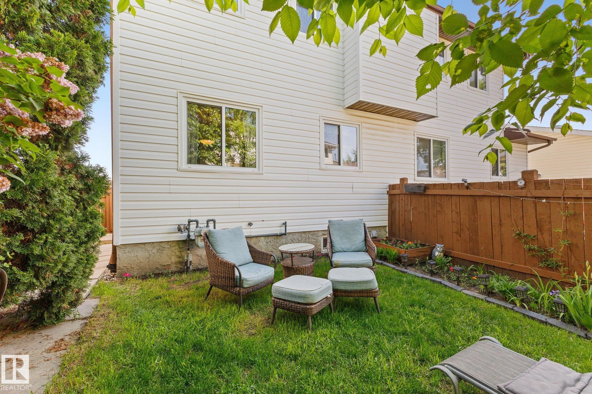Manicured lawn area with a privacy fence, multiple windows, and a raised garden bed - 17132 103 Street Nw, Edmonton, AB