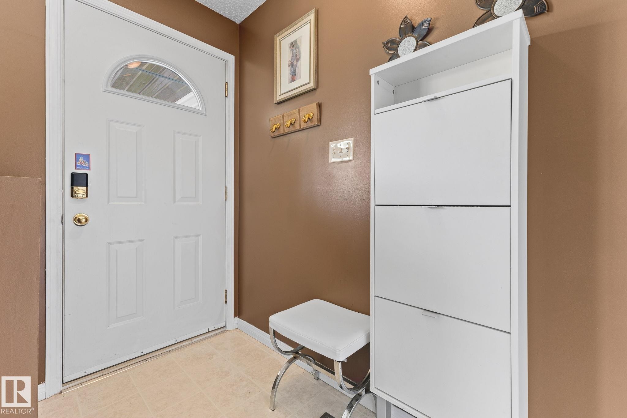 Entryway featuring a paneled door with an arched window, a digital door lock, and a light-toned tile floor - 17132 103 Street Nw, Edmonton, AB