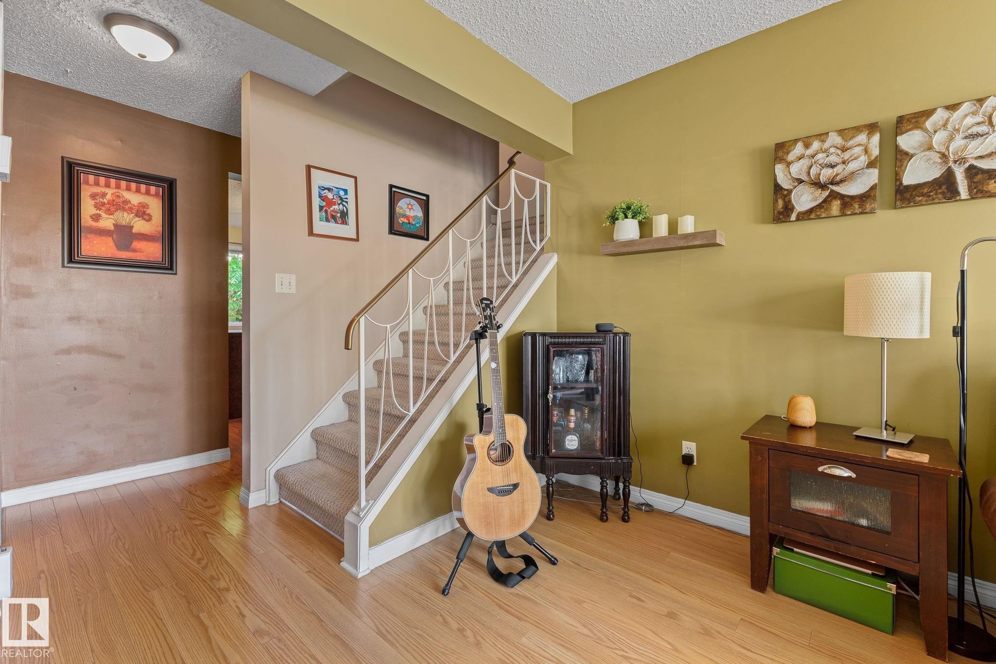 Wood-finish flooring, staircase with carpeted treads, white metal balusters, and a wood handrail - 17132 103 Street Nw, Edmonton, AB