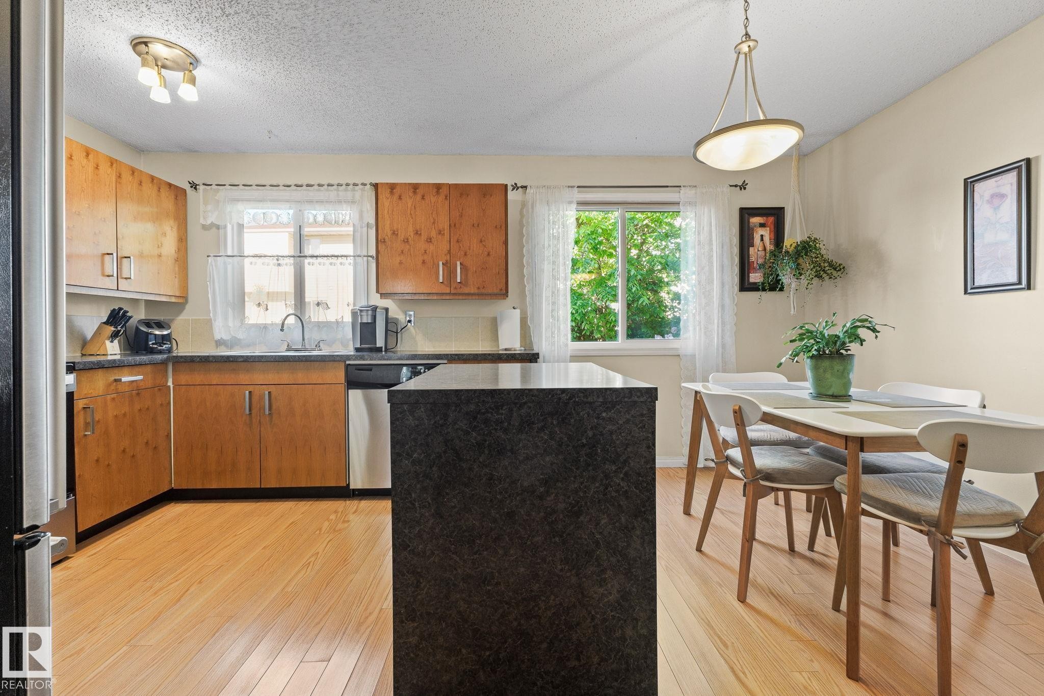 Kitchen and dining area featuring wood-finish flooring, built-in wooden cabinetry, dark countertops, and a central island - 17132 103 Street Nw, Edmonton, AB