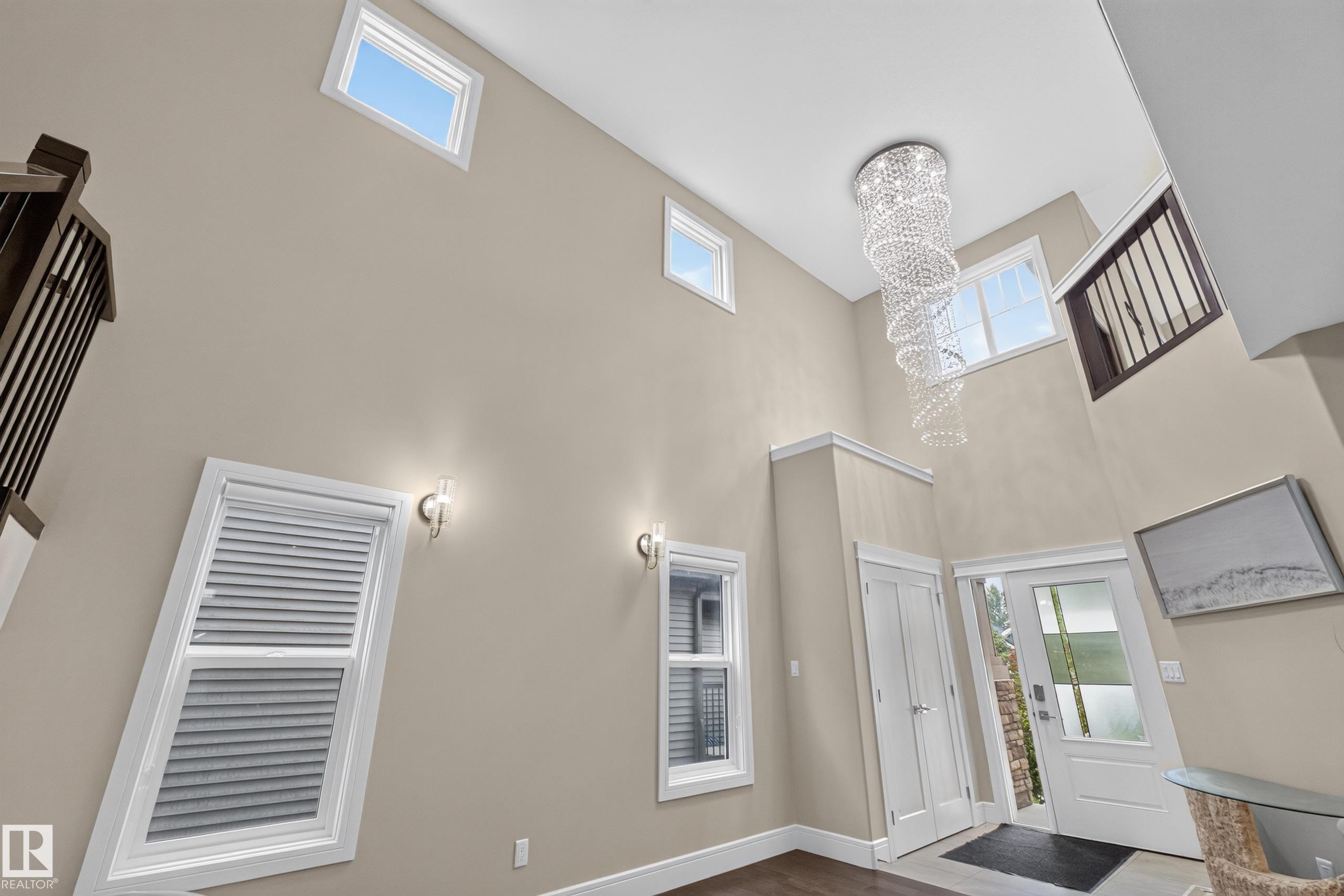 Two-story foyer with a tiered crystal chandelier, multiple windows, double doors, and dark wood-finish flooring - 7014 Chivers Loop Sw, Edmonton, AB
