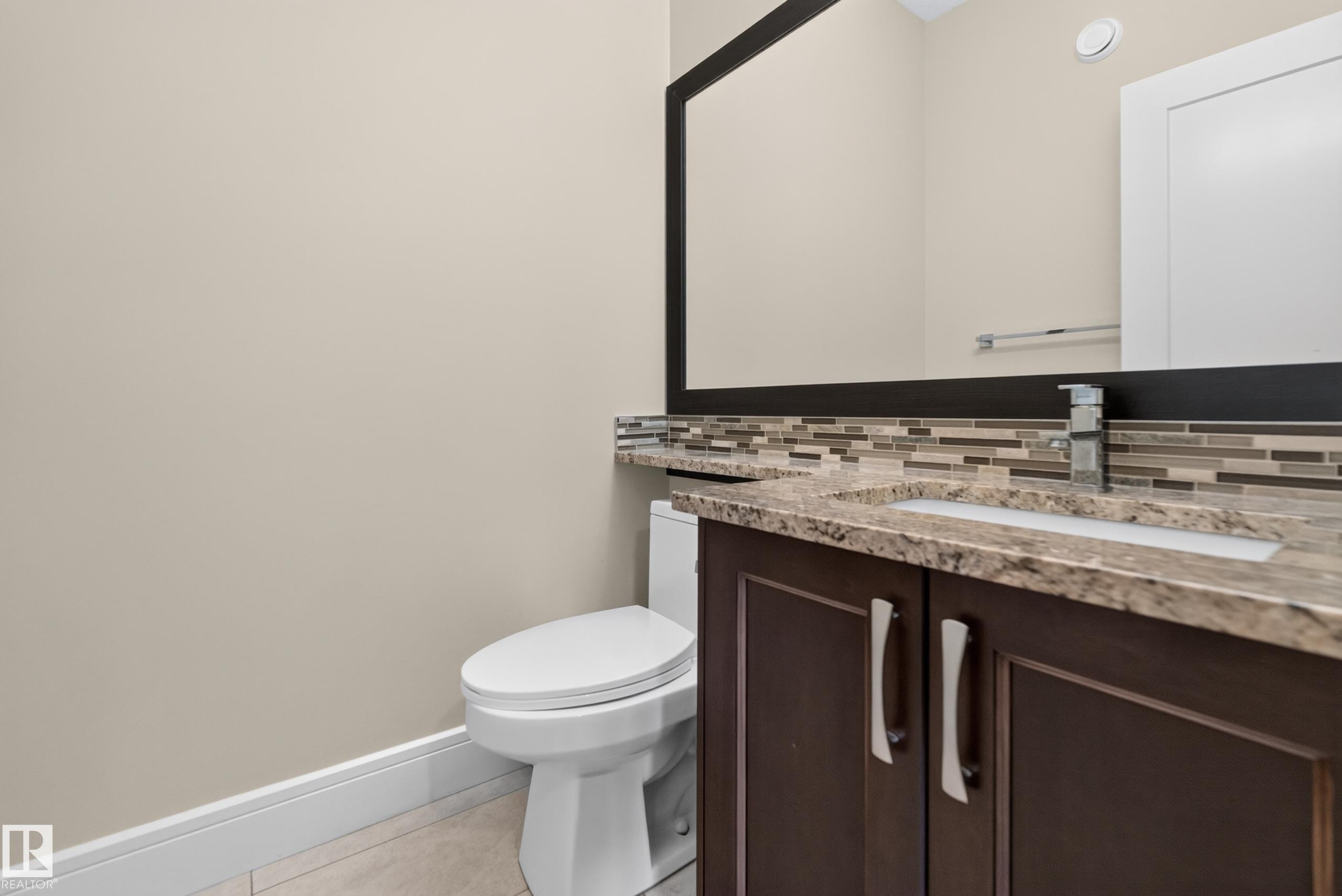 Dark wood-finish vanity with stone countertop, undermount sink, and mosaic tile backsplash - 7014 Chivers Loop Sw, Edmonton, AB