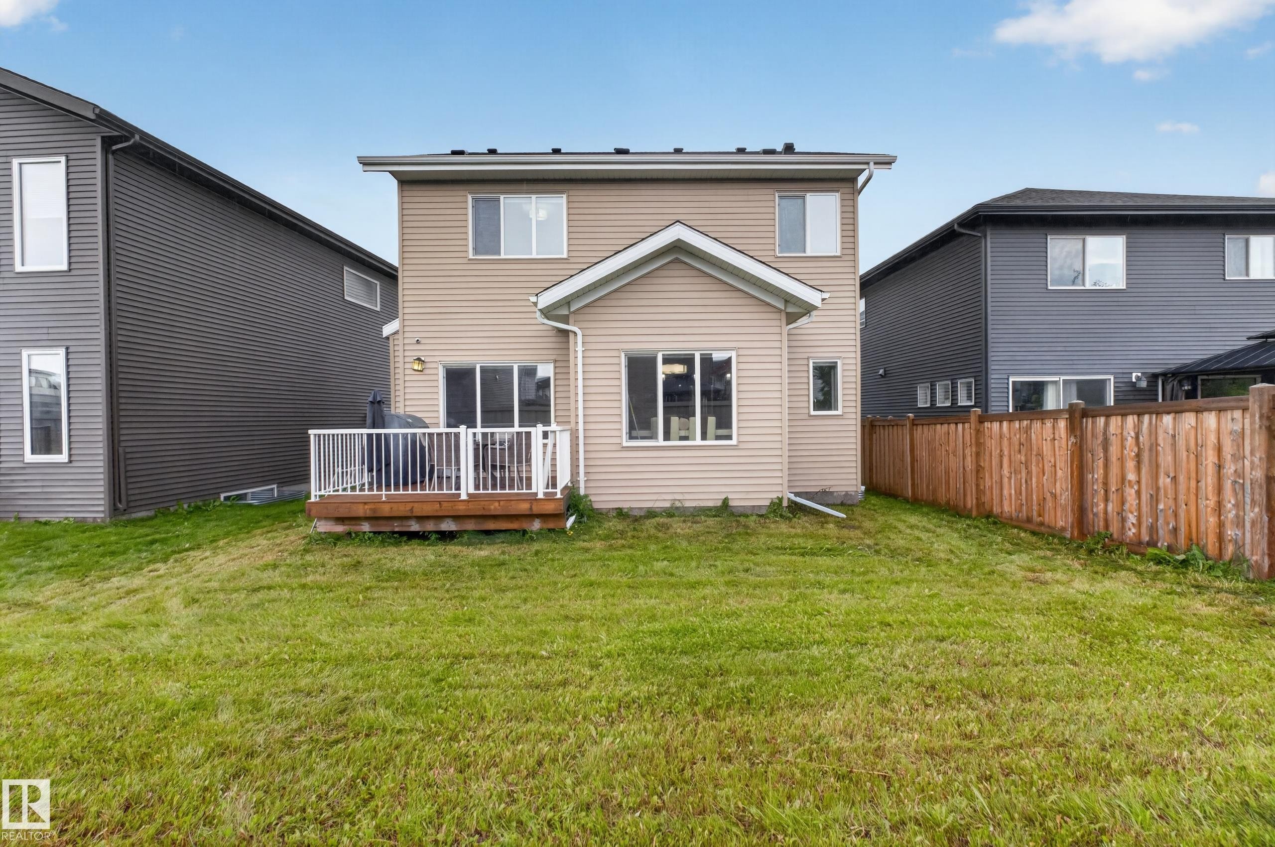 Expansive backyard featuring a wood deck with white railing, sliding glass door access, and a wood fence - 7014 Chivers Loop Sw, Edmonton, AB