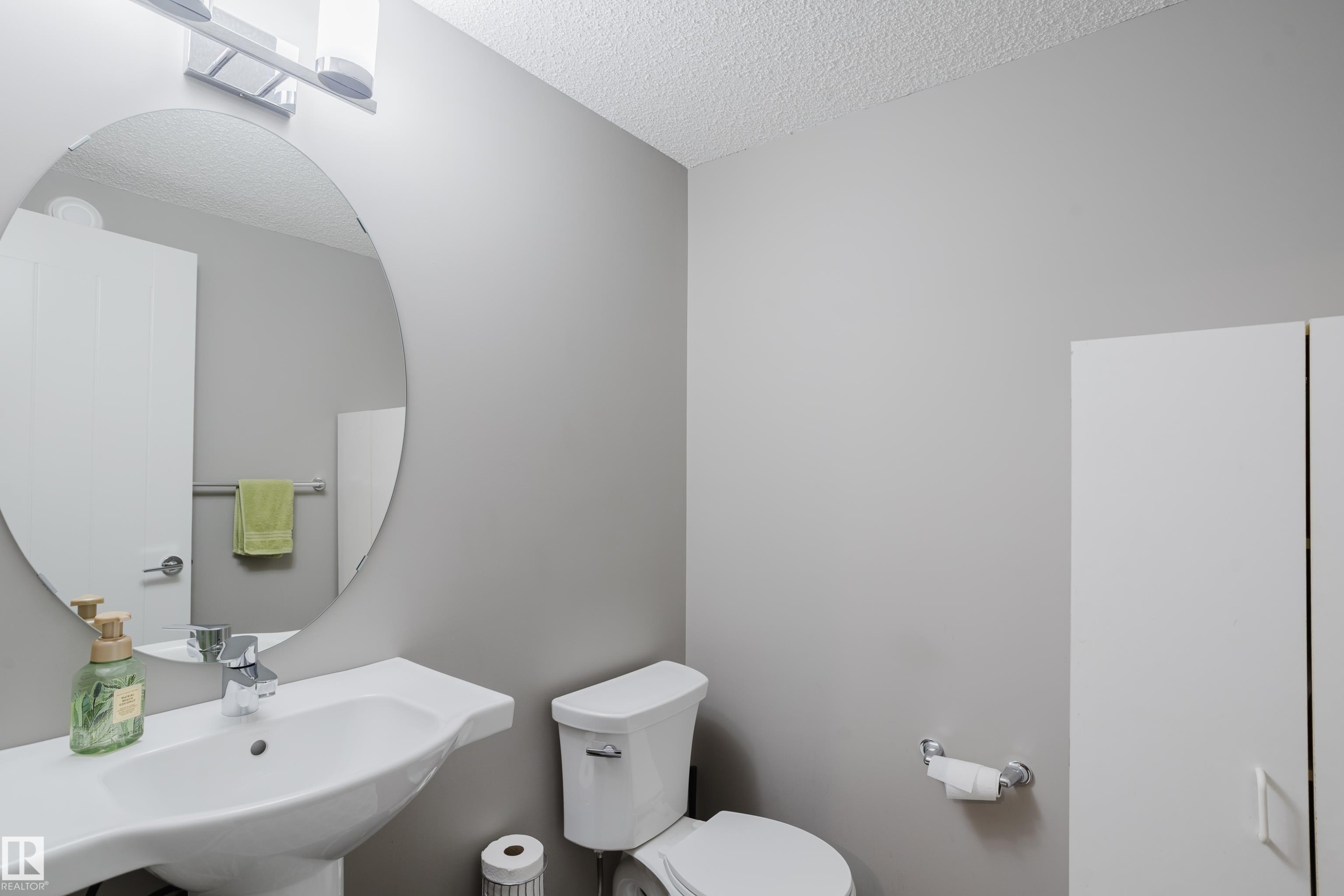 Pedestal sink with chrome faucet, oval mirror, and contemporary light fixture - #28 2215 24 St Nw, Edmonton, AB - Indoor Photo Showing Bathroom