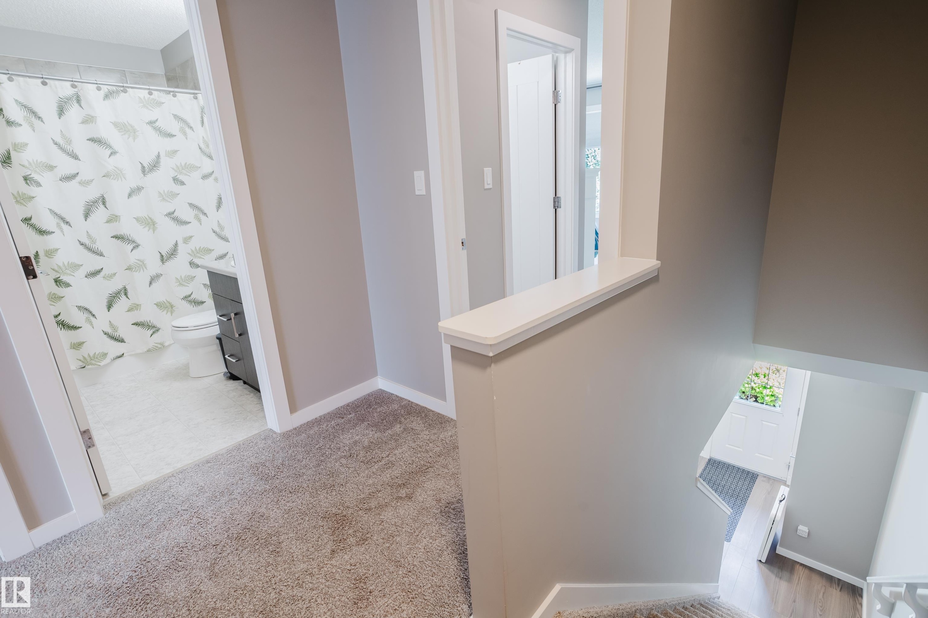 Carpeted hallway with a neutral color palette, white baseboards, and a partial wall overlooking a lower level - #28 2215 24 St Nw, Edmonton, AB - Indoor Photo Showing Other Room