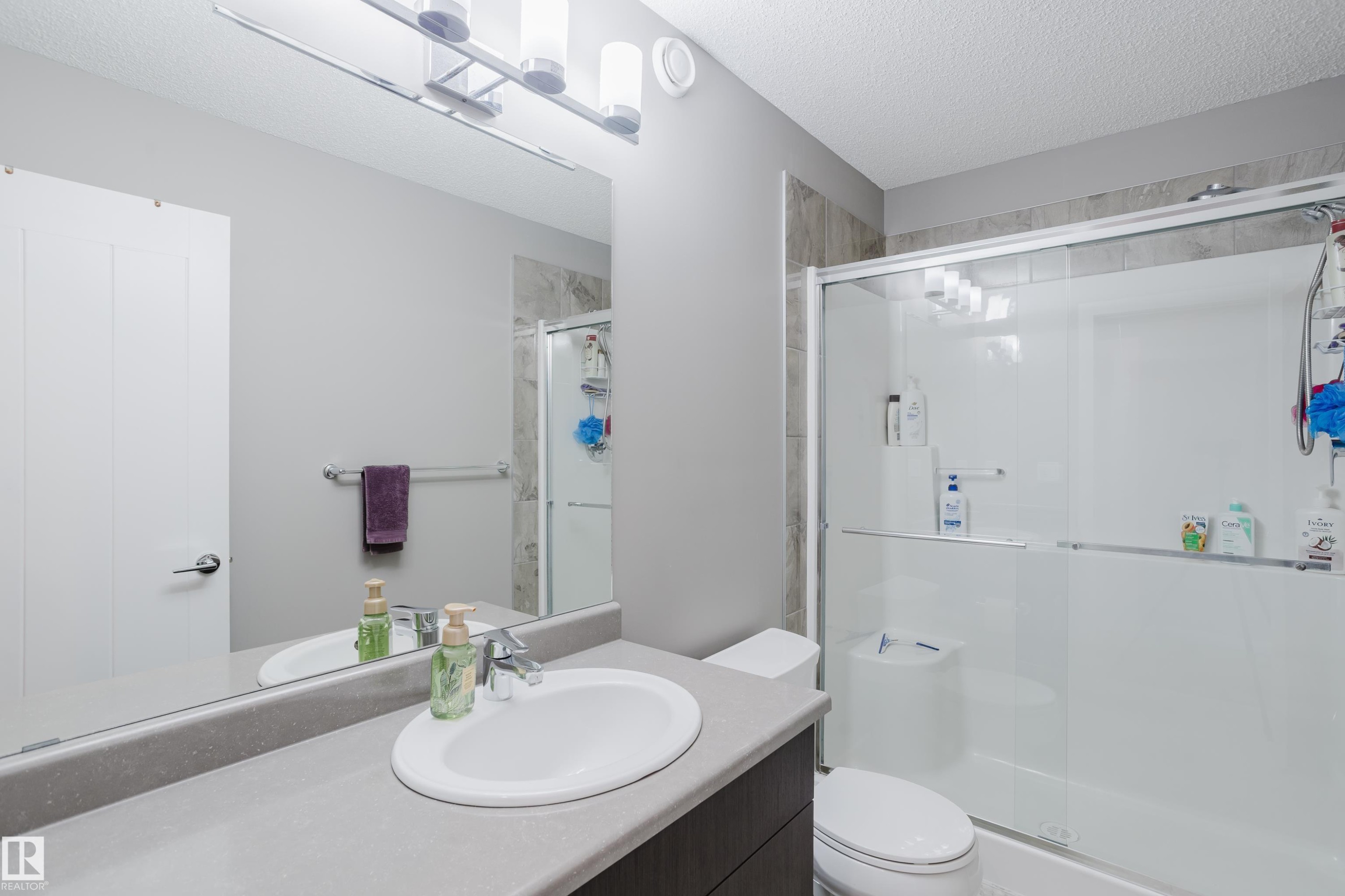 Bathroom featuring a vanity with an integrated sink, a large wall-mounted mirror, and a shower with sliding glass doors - #28 2215 24 St Nw, Edmonton, AB - Indoor Photo Showing Bathroom