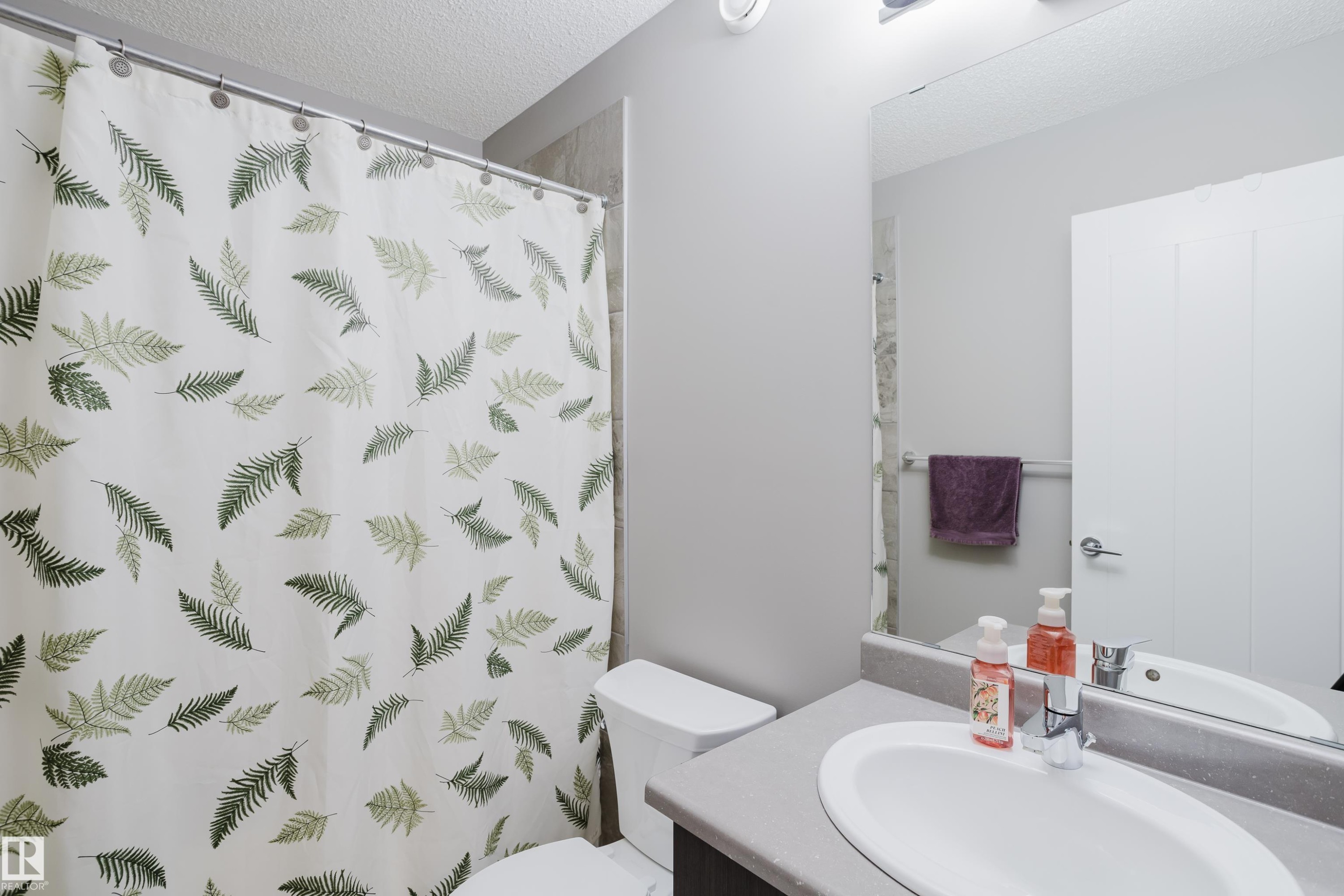 Bathroom featuring a white toilet, an integrated sink with a chrome faucet, and a large wall-mounted mirror - #28 2215 24 St Nw, Edmonton, AB - Indoor Photo Showing Bathroom