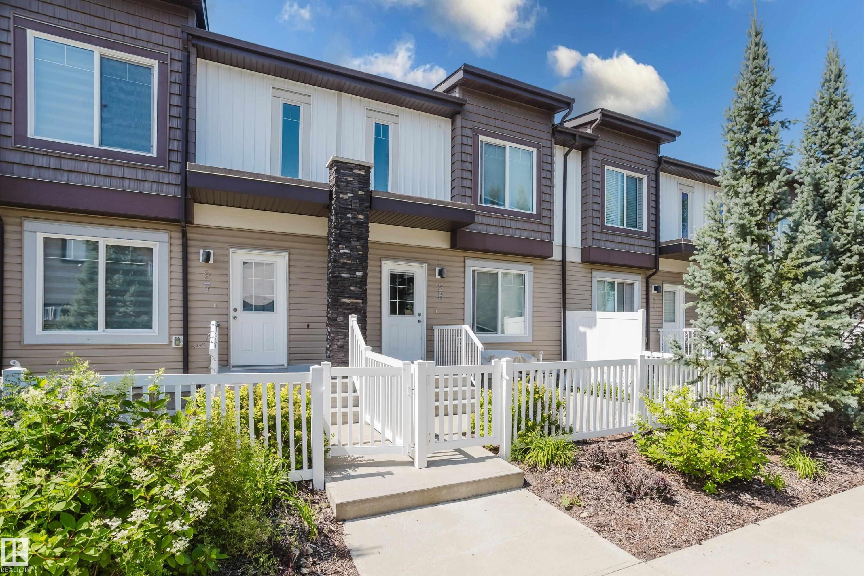 Contemporary townhome exterior featuring multi-toned siding, white trim, and a prominent stone accent column - #28 2215 24 St Nw, Edmonton, AB - Outdoor With Facade