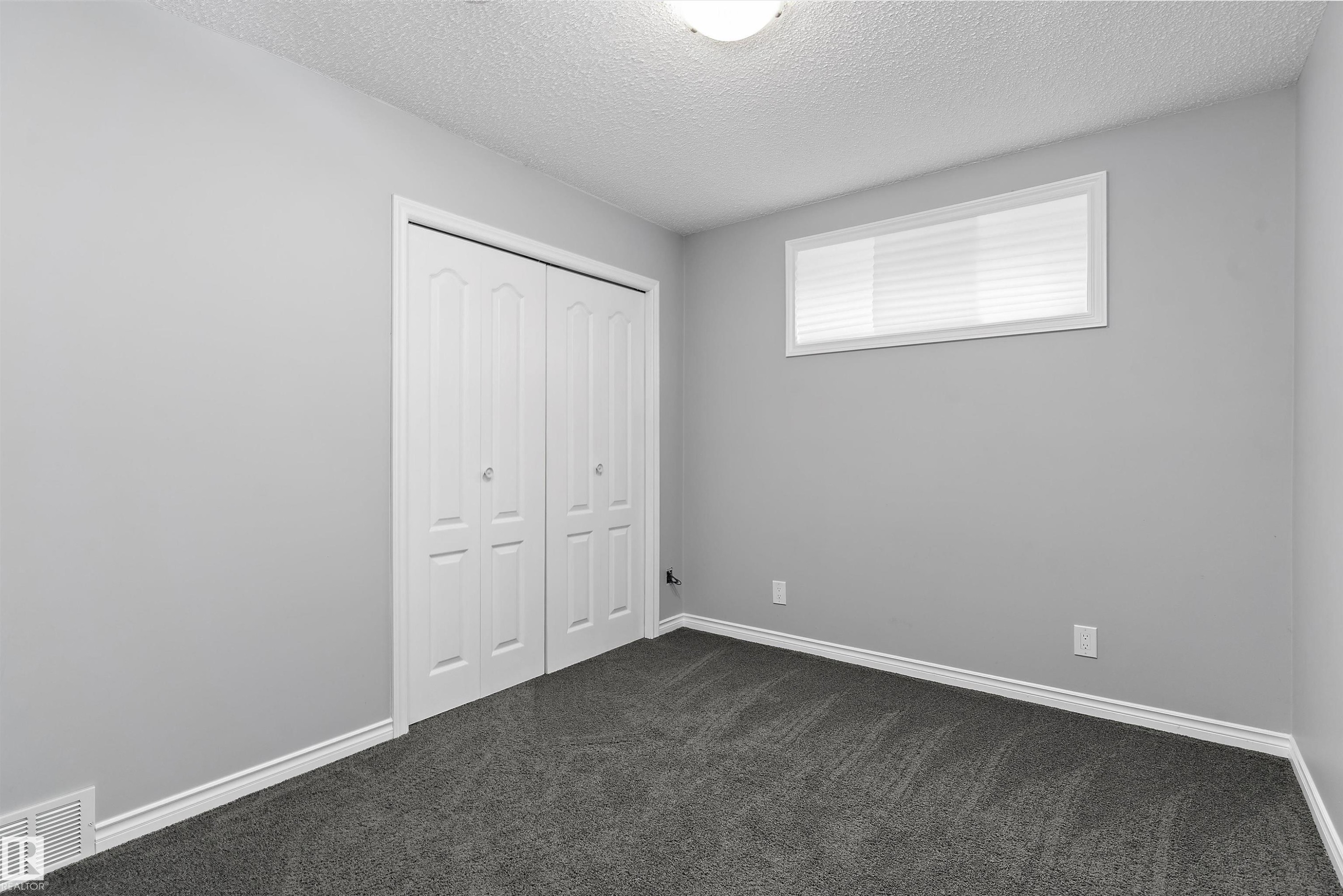 Recessed window with white blinds, neutral wall paint, white bi-fold closet doors, and plush dark gray carpeting - 20845 92A Avenue Nw, Edmonton, AB - Indoor Photo Showing Other Room