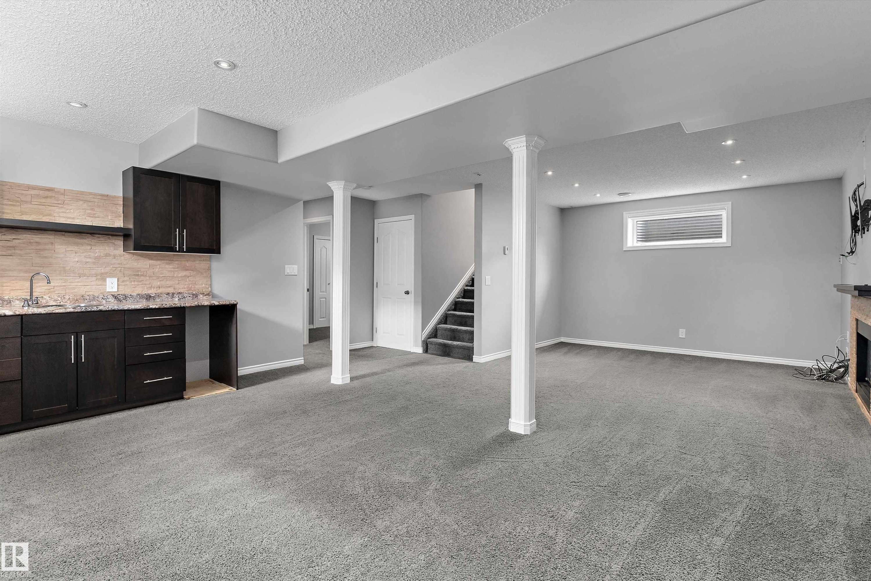 Spacious room with plush carpeting, recessed lighting, and a built-in wet bar featuring a sink, dark cabinetry, and stone-finish countertop - 20845 92A Avenue Nw, Edmonton, AB - Indoor