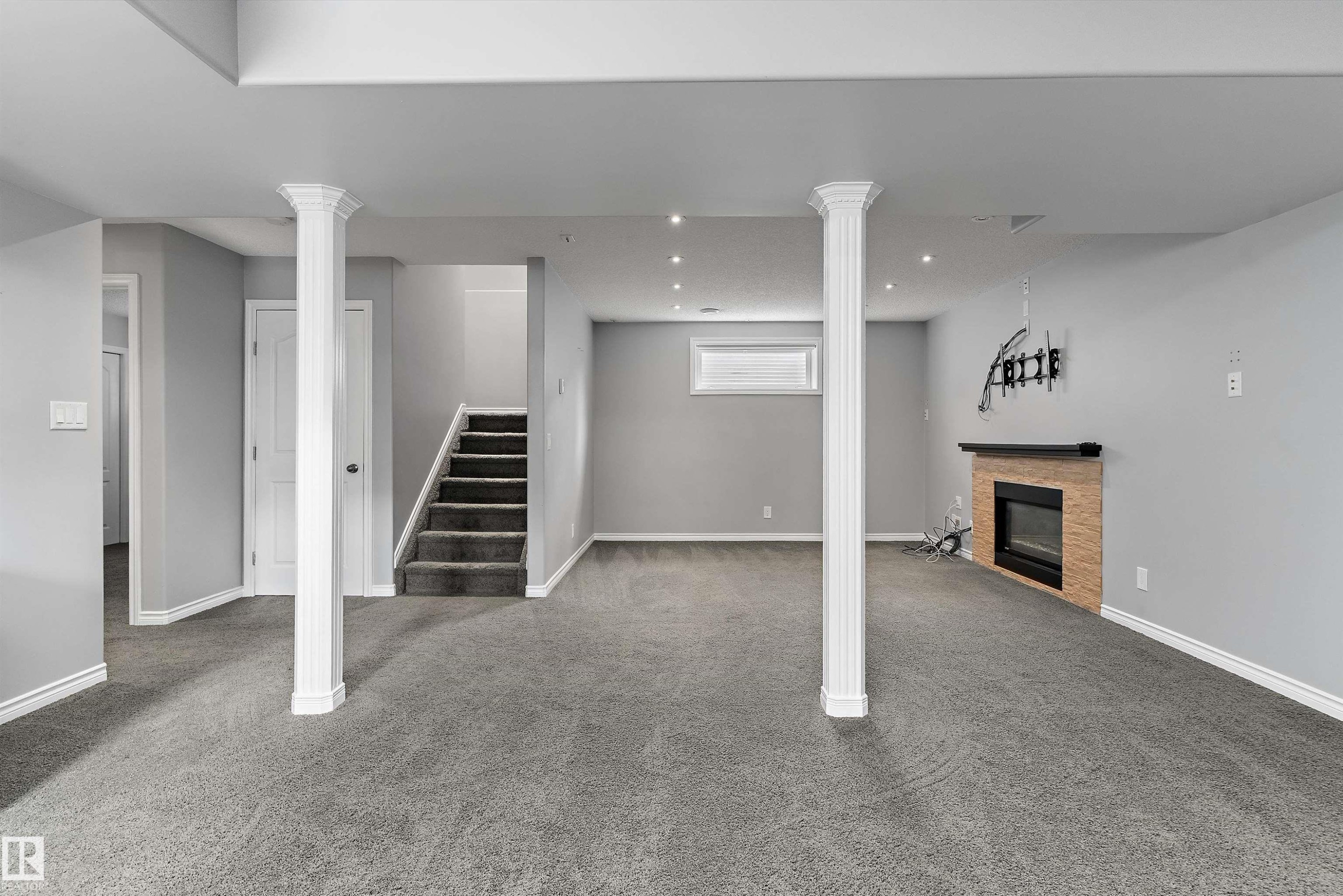 Spacious lower-level area featuring recessed lighting, a built-in fireplace with a stone surround, and carpeted flooring - 20845 92A Avenue Nw, Edmonton, AB - Indoor With Fireplace