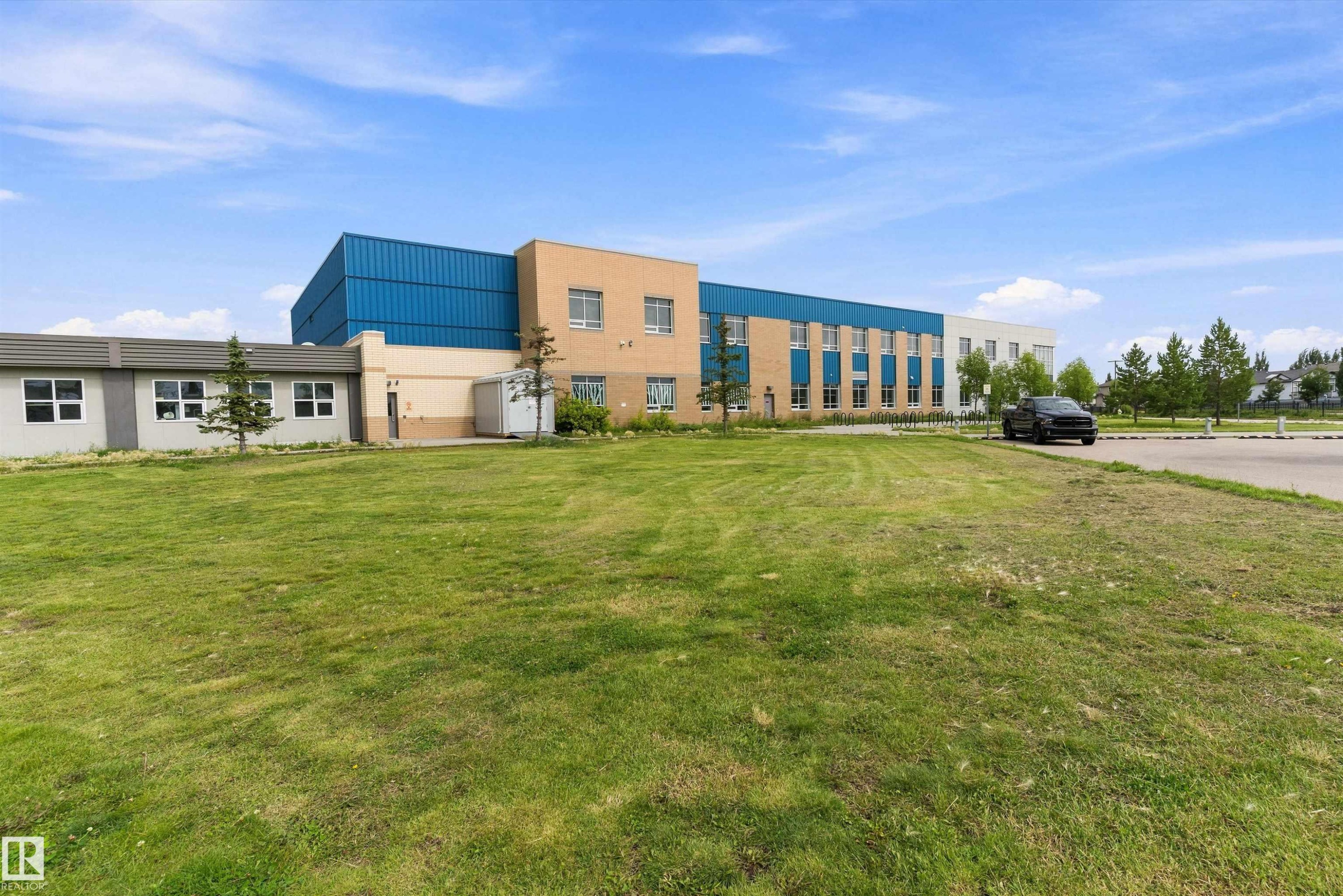 Exterior building featuring a combination of brick, metal siding, and stucco finishes, multiple window installations, and a surrounding green space - 20845 92A Avenue Nw, Edmonton, AB - Outdoor