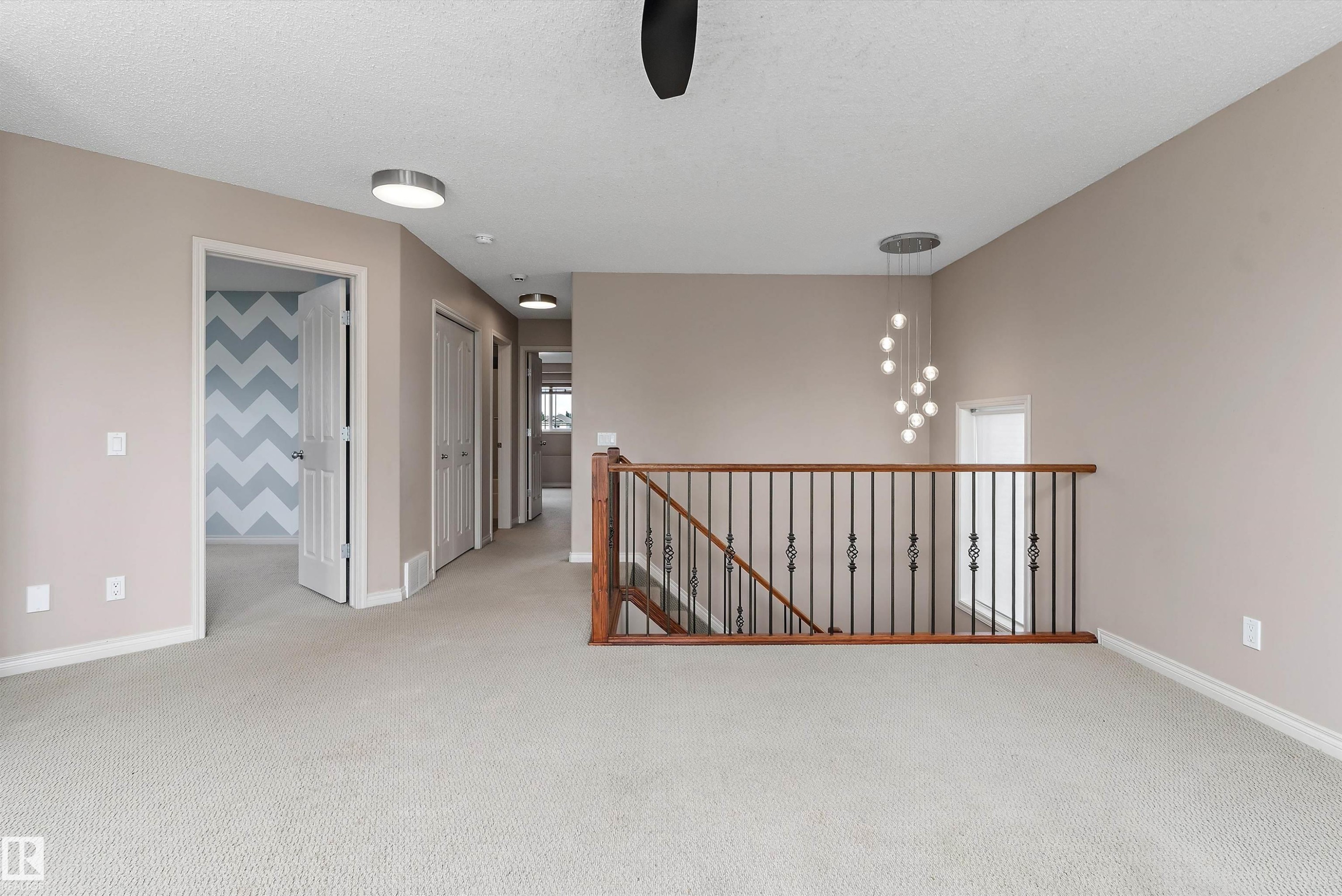 Carpeted flooring throughout, with a wood and wrought iron staircase railing, and a contemporary chandelier - 20845 92A Avenue Nw, Edmonton, AB - Indoor Photo Showing Other Room