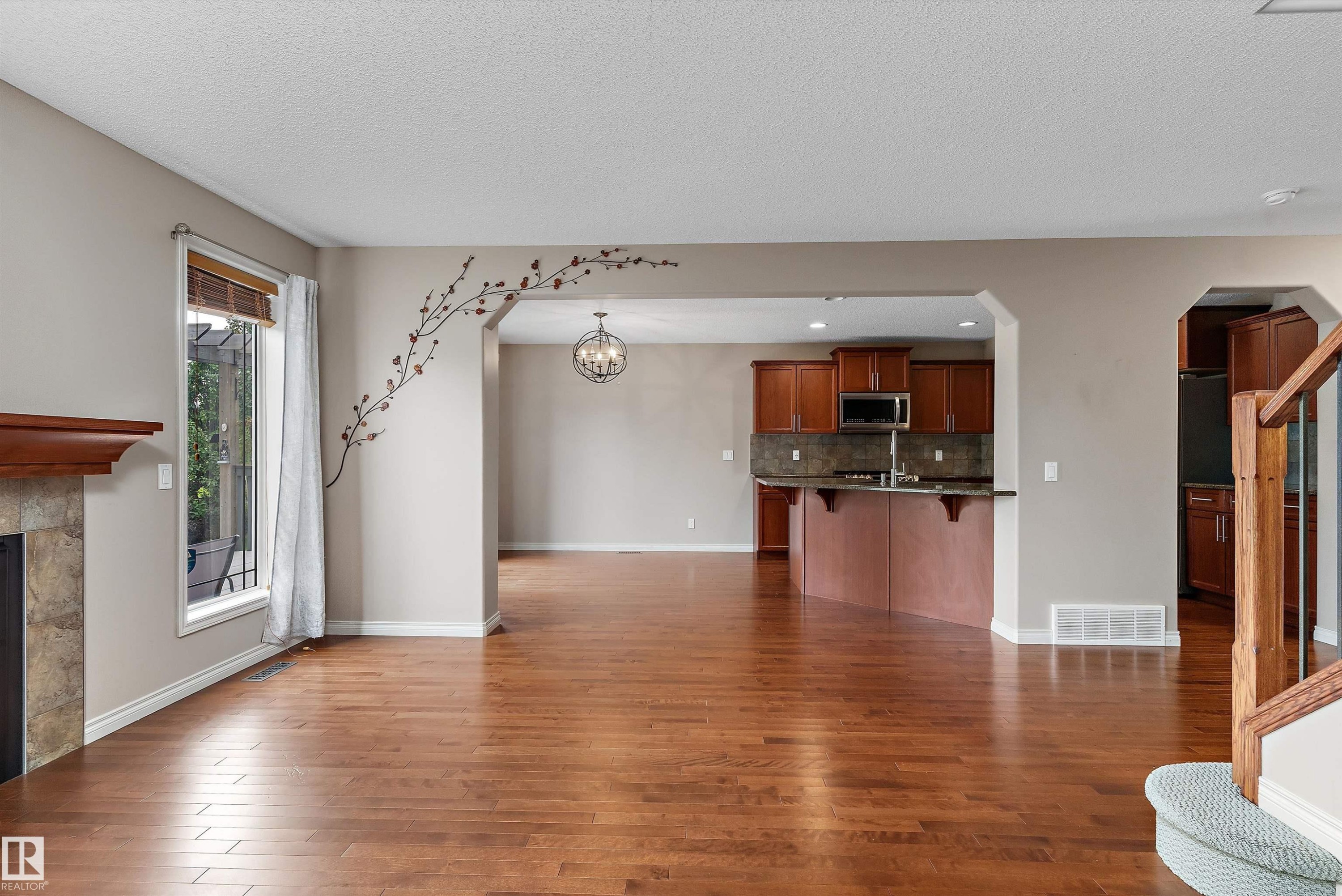 Wood-finish flooring throughout, fireplace with a stone surround and wood mantel, arched entryways, kitchen with wood cabinetry and stainless steel appliances, and a built-in kitchen island - 20845 92A Avenue Nw, Edmonton, AB - Indoor With Fireplace