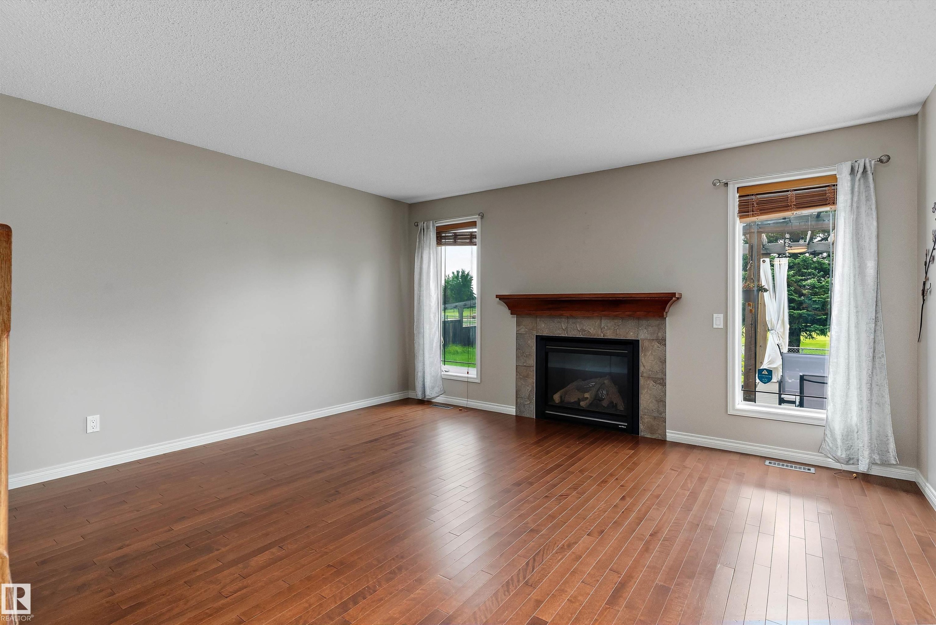 Hardwood-style flooring, stone-clad fireplace with wood mantel, and multiple windows - 20845 92A Avenue Nw, Edmonton, AB - Indoor Photo Showing Living Room With Fireplace