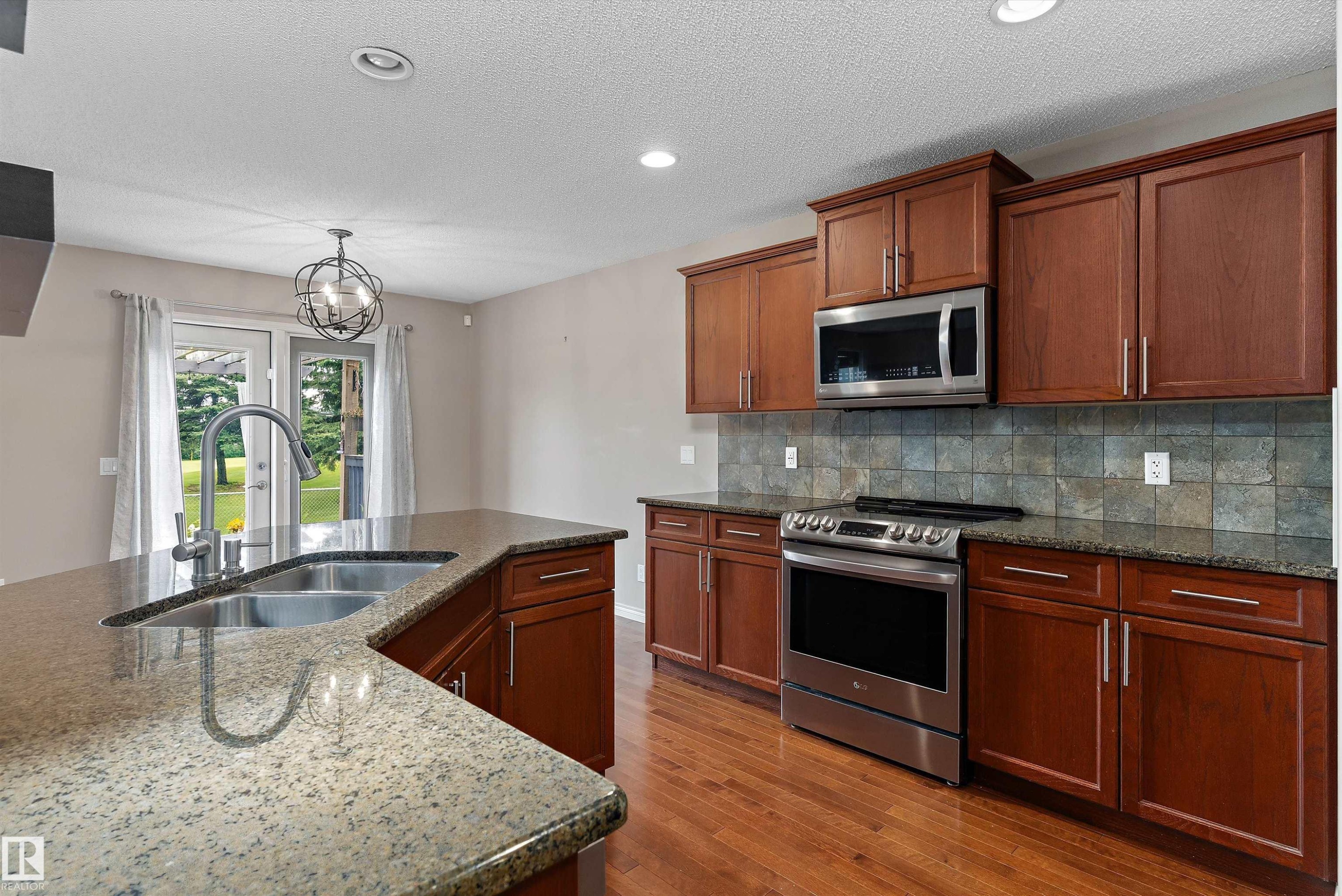 Kitchen featuring wood cabinetry, stainless steel appliances, stone countertops, and a tile backsplash - 20845 92A Avenue Nw, Edmonton, AB - Indoor Photo Showing Kitchen With Double Sink