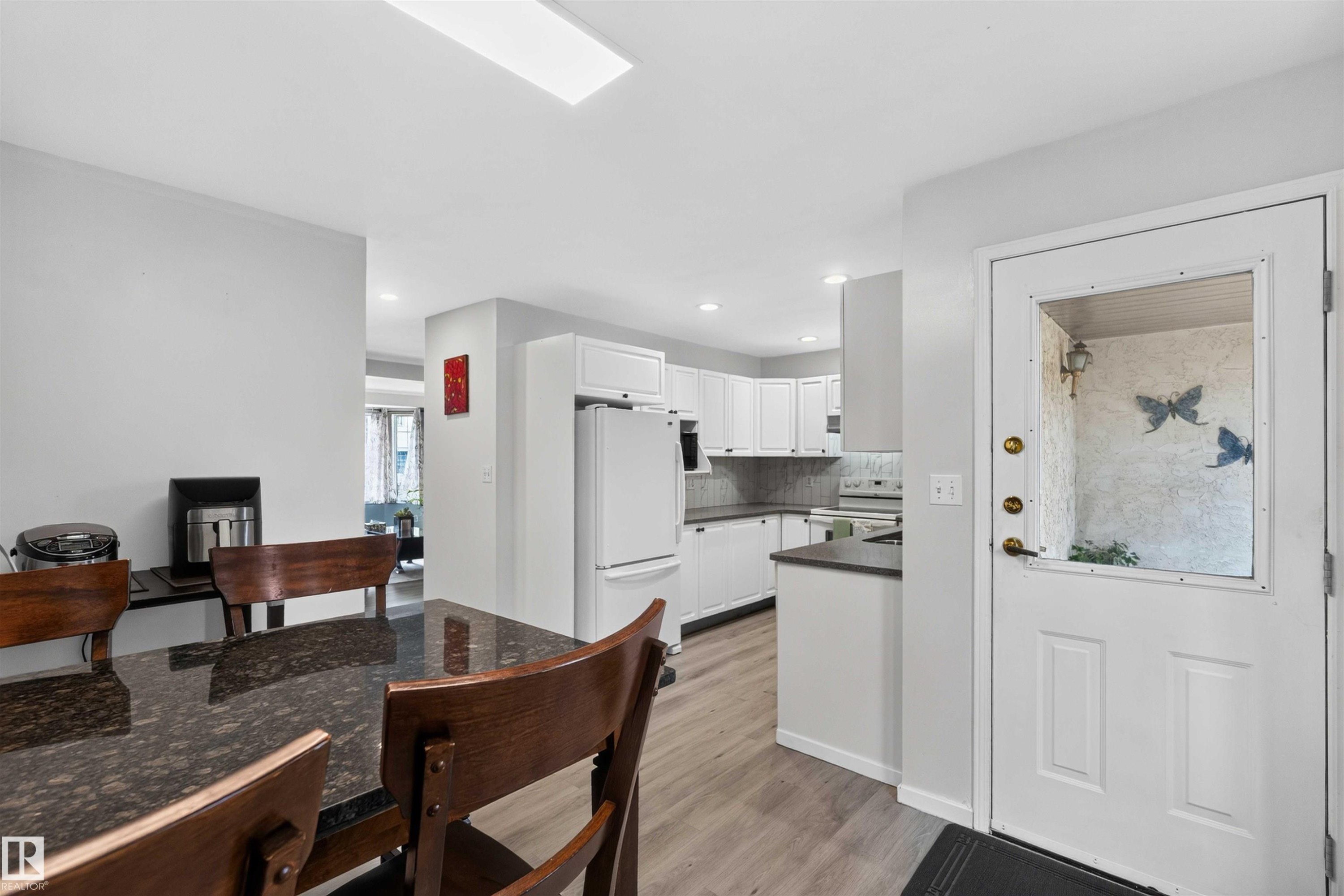 Open-concept living area featuring wood-finish flooring, white cabinetry, dark countertops, and a white refrigerator - #28 3645 145 Av Nw, Edmonton, AB - Indoor Photo Showing Kitchen