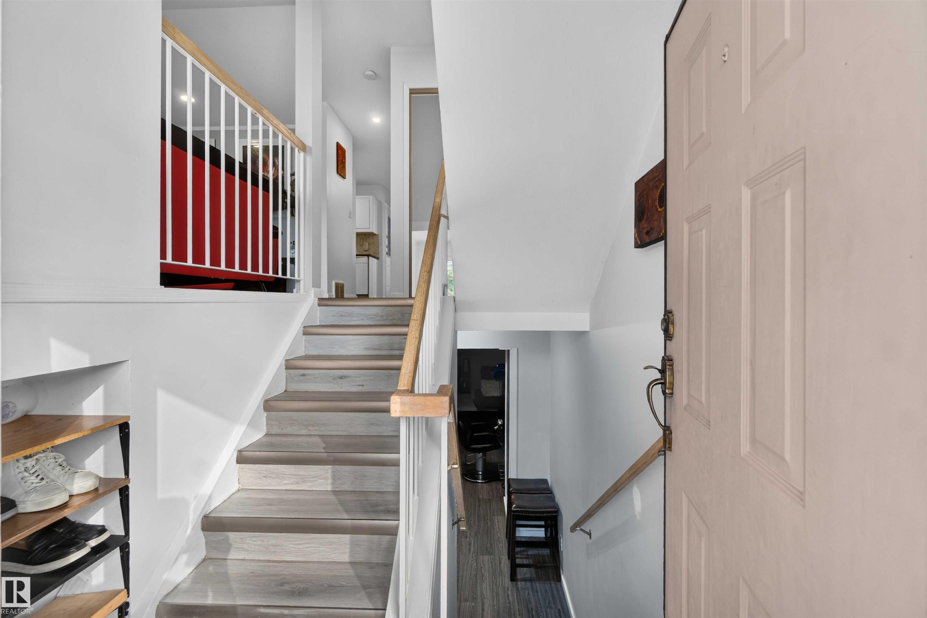 Wood-finish flooring on stairs, white baluster railing, natural wood handrails, and a paneled entry door with brass hardware - #28 3645 145 Av Nw, Edmonton, AB - Indoor Photo Showing Other Room