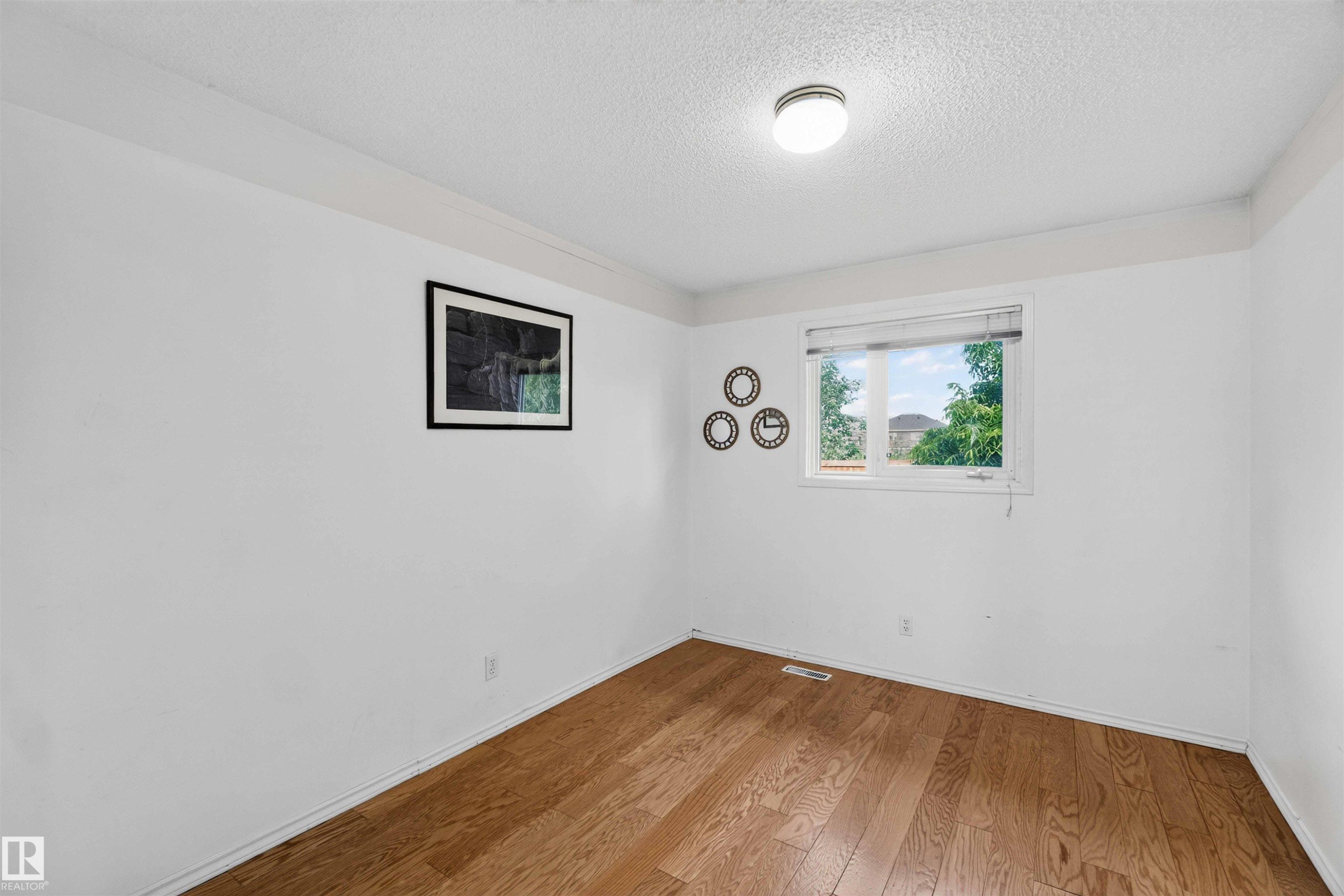 Wood-finish flooring with white baseboards, a white ceiling, and a flush mount light fixture - #28 3645 145 Av Nw, Edmonton, AB - Indoor Photo Showing Other Room