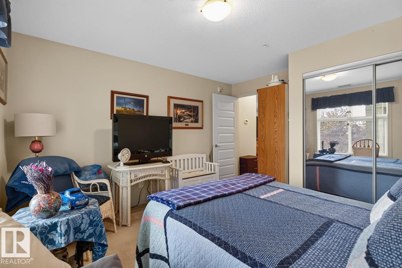 Mirrored closet doors, flush-mount ceiling light fixture, neutral wall color, white interior door, wood-finish cabinetry - #210 7909 71 St Nw, Edmonton, AB - Indoor Photo Showing Bedroom