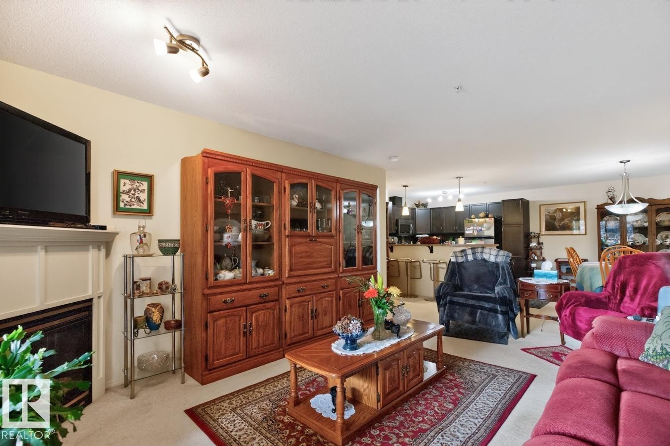 Neutral wall paint, carpeted flooring, track lighting, and a built-in fireplace - #210 7909 71 St Nw, Edmonton, AB - Indoor Photo Showing Living Room With Fireplace
