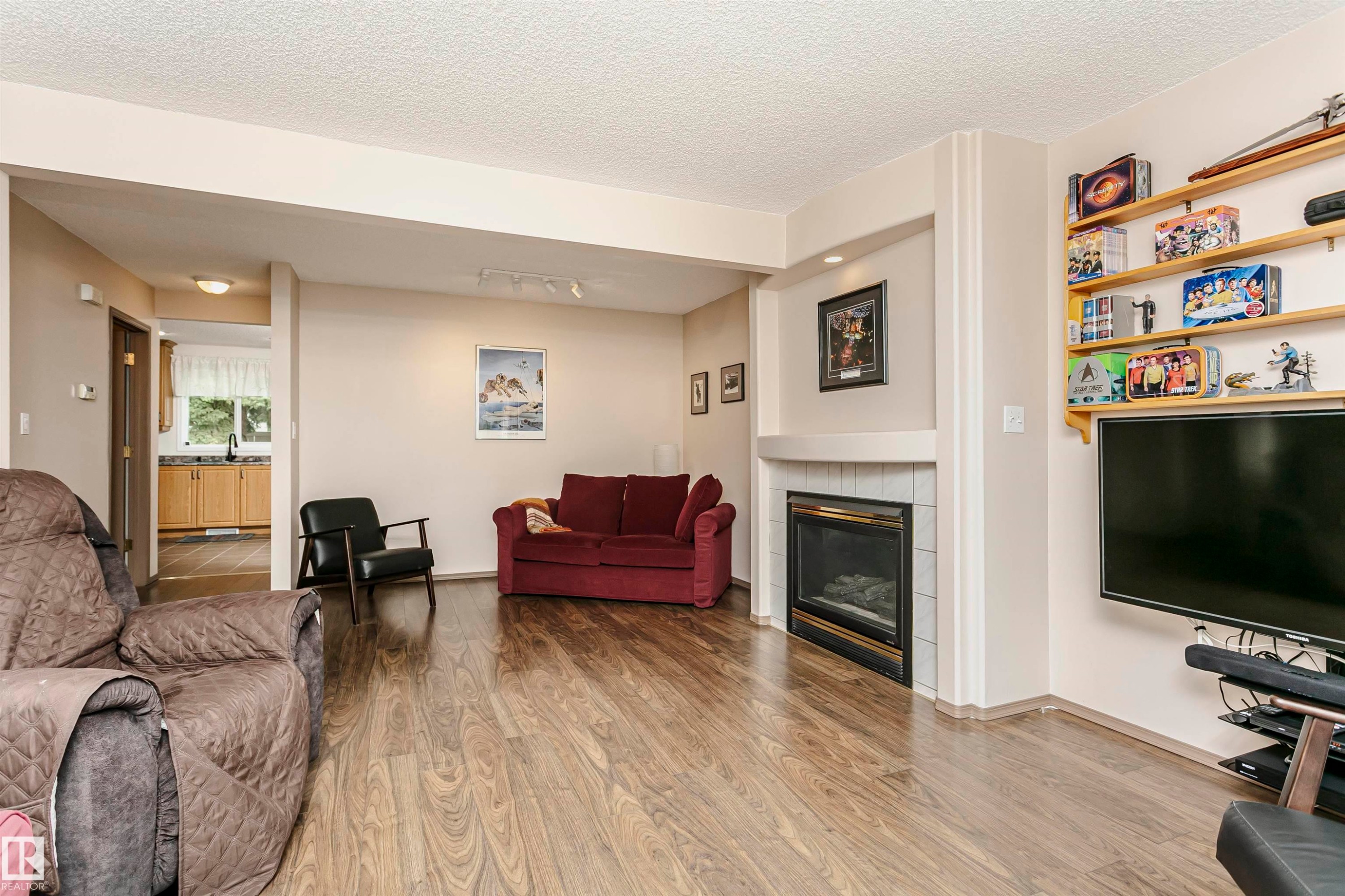 Wood-finish flooring throughout, recessed lighting, and a white tile-surround fireplace with a black insert - #42 9630 176 St Nw, Edmonton, AB - Indoor Photo Showing Living Room With Fireplace