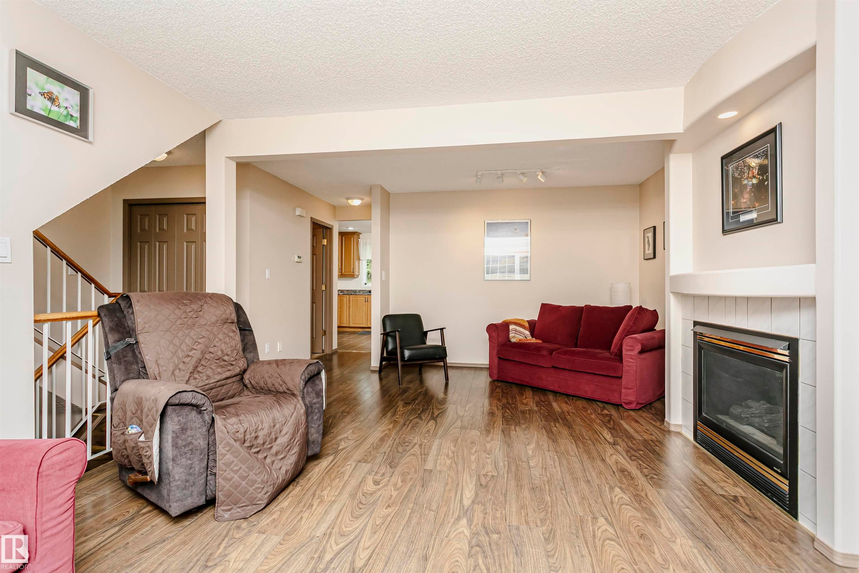 Wood-finish flooring, staircase with white spindles, gas fireplace with white tile surround, recessed lighting, and a neutral color palette - #42 9630 176 St Nw, Edmonton, AB - Indoor Photo Showing Living Room With Fireplace