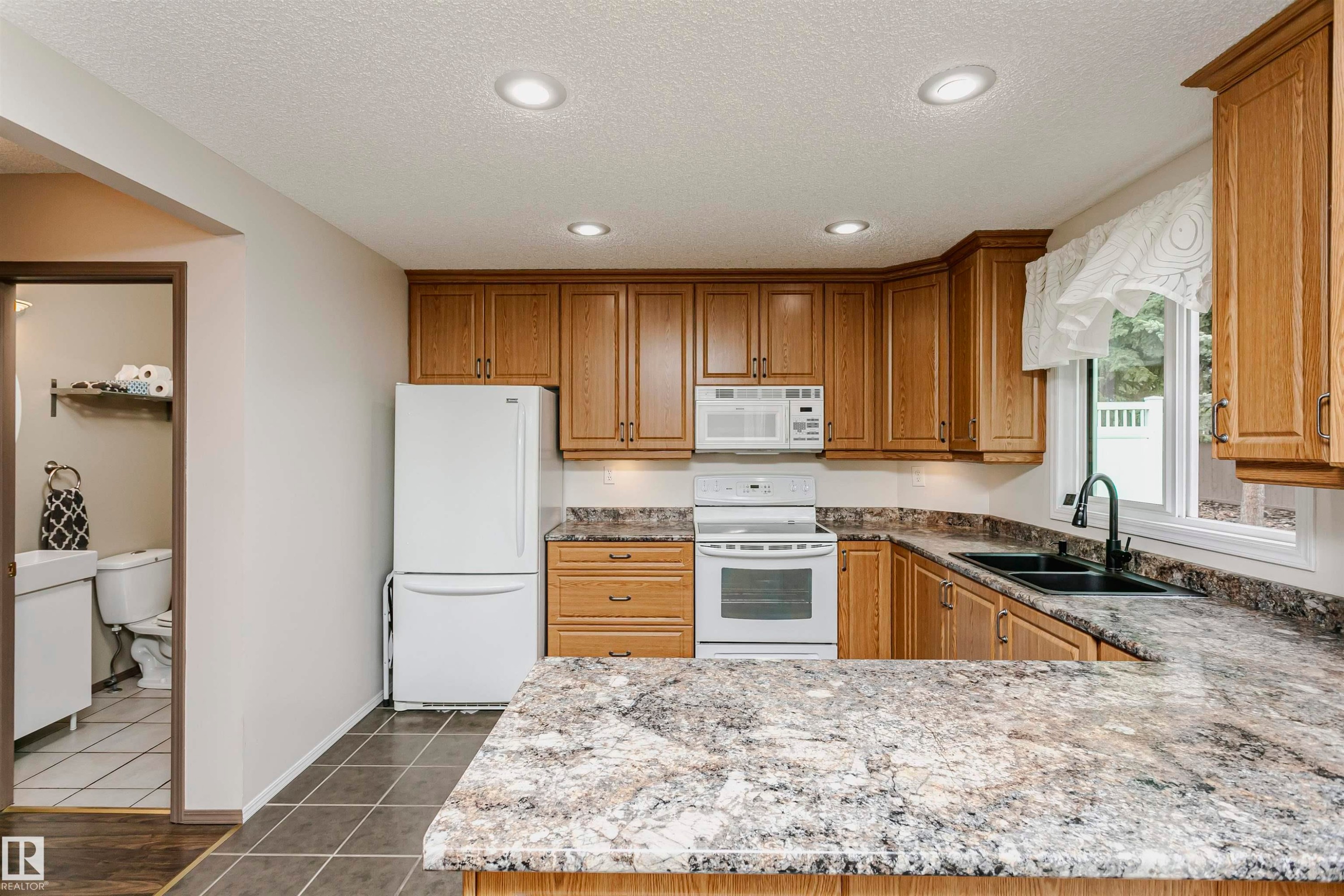 Kitchen featuring wood cabinetry, light-toned countertops, tile flooring, and recessed lighting - #42 9630 176 St Nw, Edmonton, AB - Indoor Photo Showing Kitchen With Double Sink
