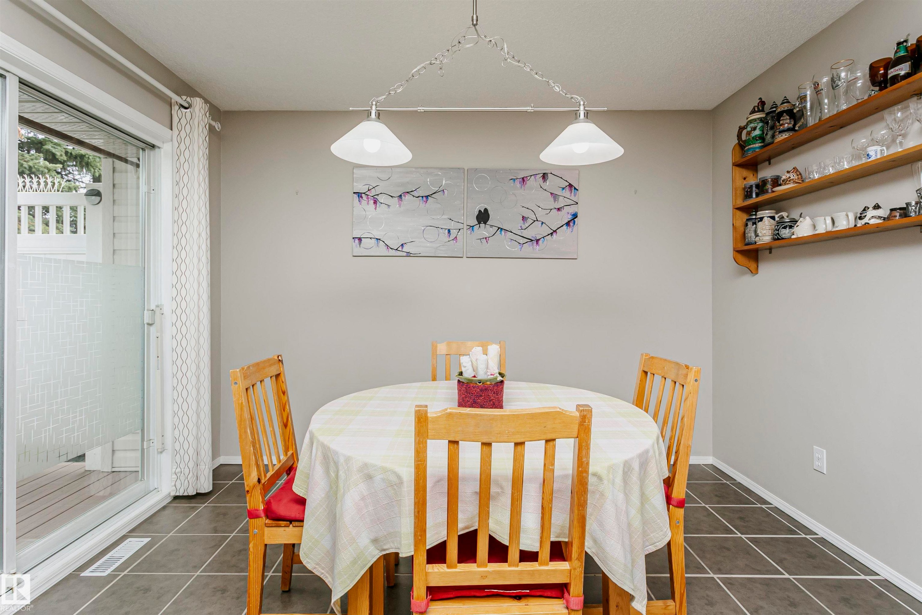 Sliding glass door to an exterior deck, square tile flooring, wood shelving, and a suspended ceiling light fixture - #42 9630 176 St Nw, Edmonton, AB - Indoor Photo Showing Dining Room