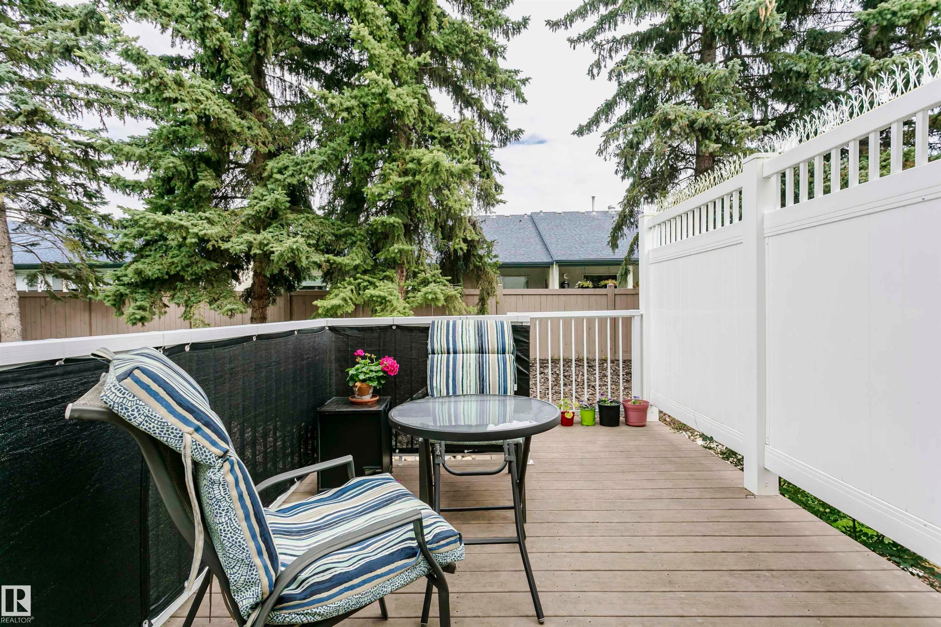 Spacious outdoor deck featuring wood-finish flooring, white privacy fencing, and mature trees - #42 9630 176 St Nw, Edmonton, AB - Outdoor With Deck Patio Veranda With Exterior