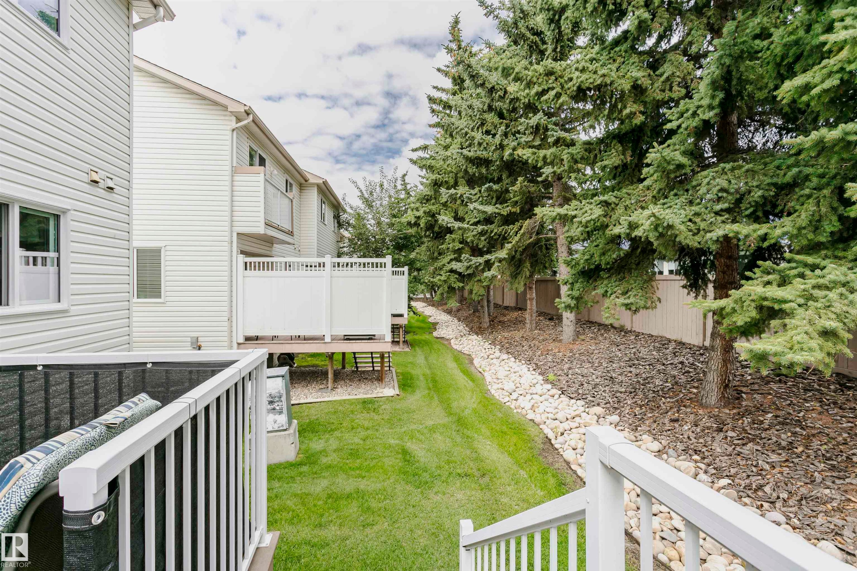Expansive backyard featuring a manicured lawn, mature evergreen trees, and a rock-lined drainage channel - #42 9630 176 St Nw, Edmonton, AB - Outdoor