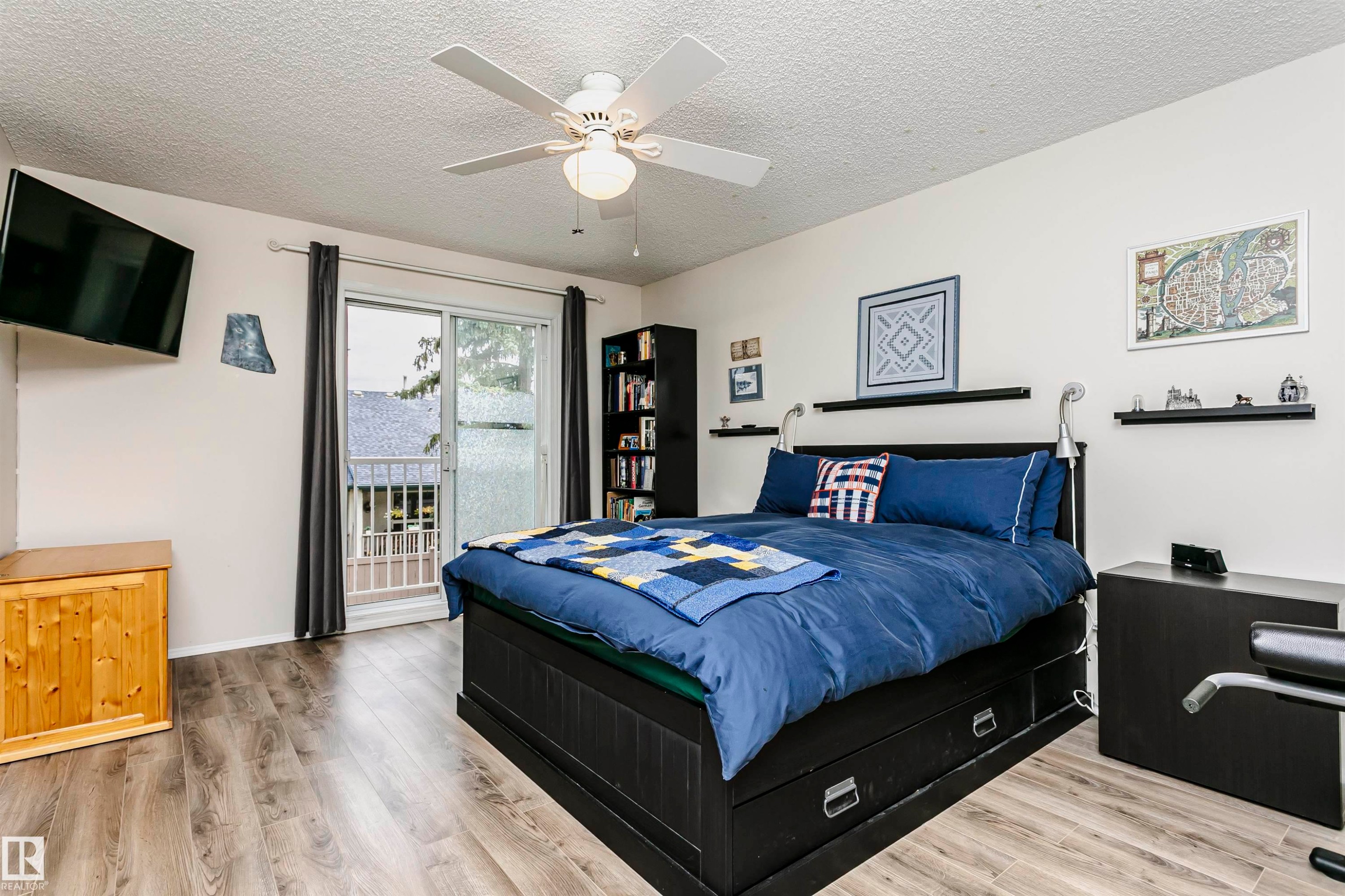 Wood-finish flooring, ceiling fan, white walls, sliding glass door, and built-in shelving - #42 9630 176 St Nw, Edmonton, AB - Indoor Photo Showing Bedroom
